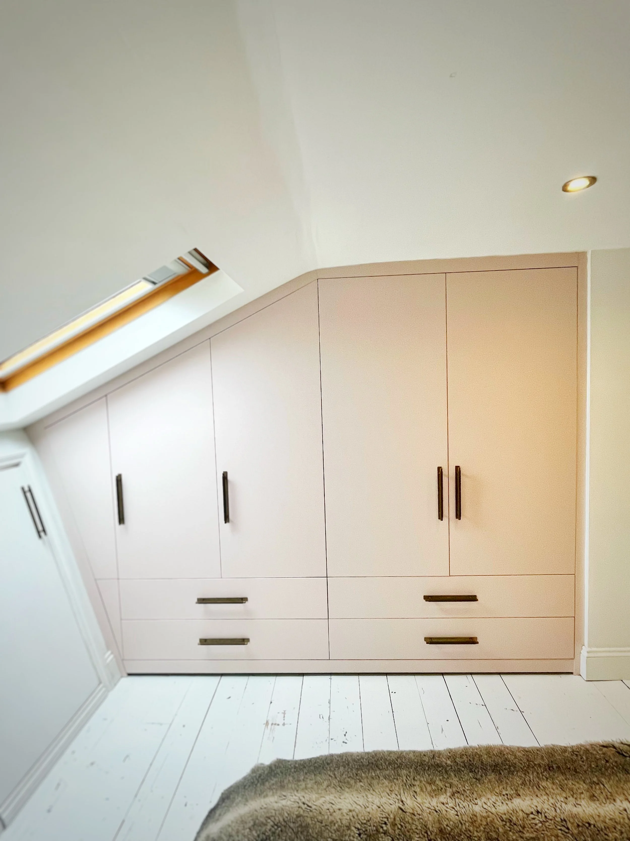 White built-in closet with black handles in a room with a sloped ceiling and skylight window.