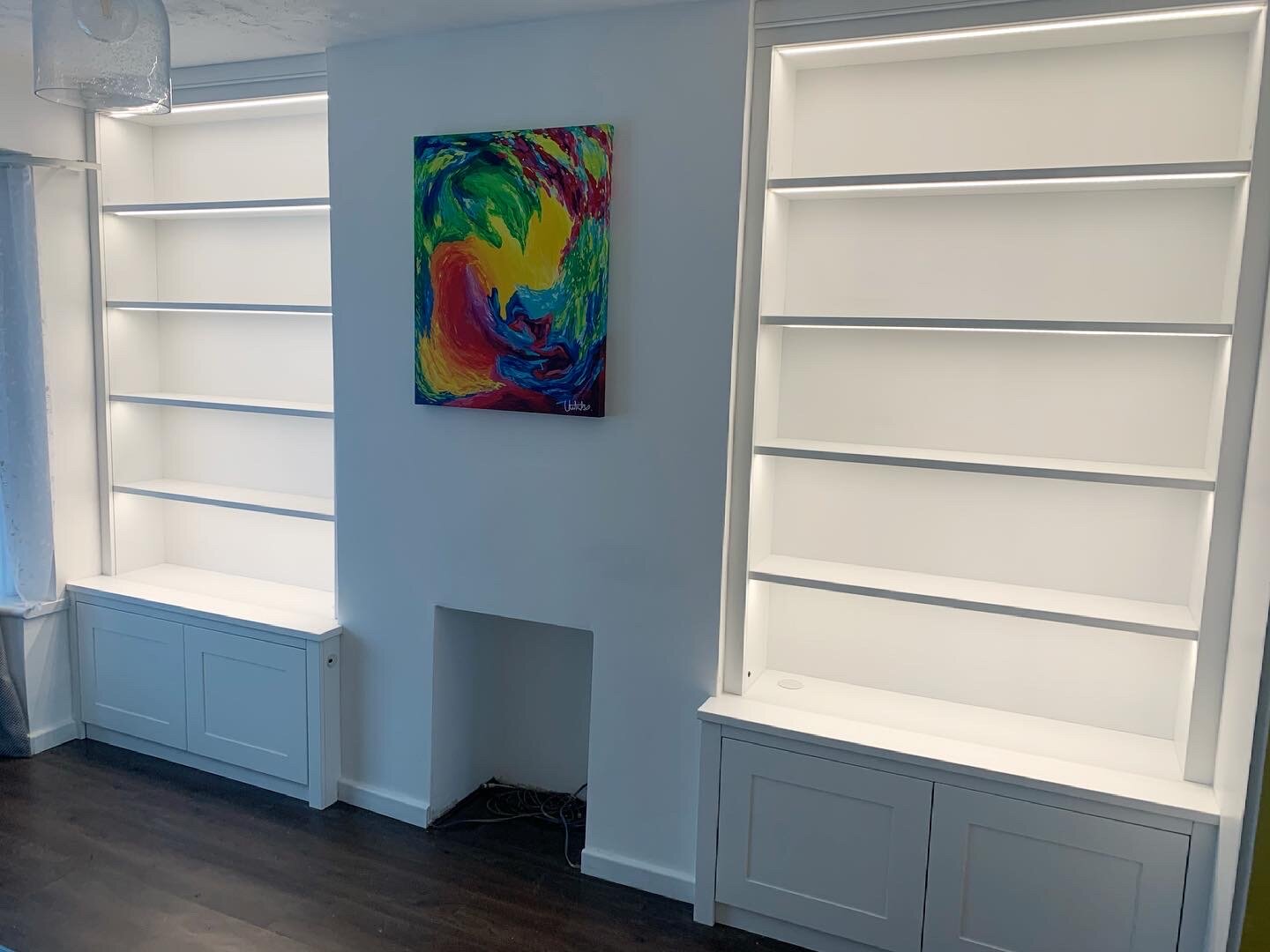 Empty white bookshelves with a colorful abstract painting on a light blue wall in a room with dark floors.