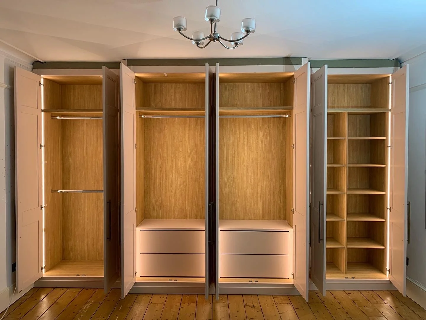 Empty built-in wooden wardrobes with open doors, showcasing shelves and hanging space, in a room with wooden floor and ceiling lamp.
