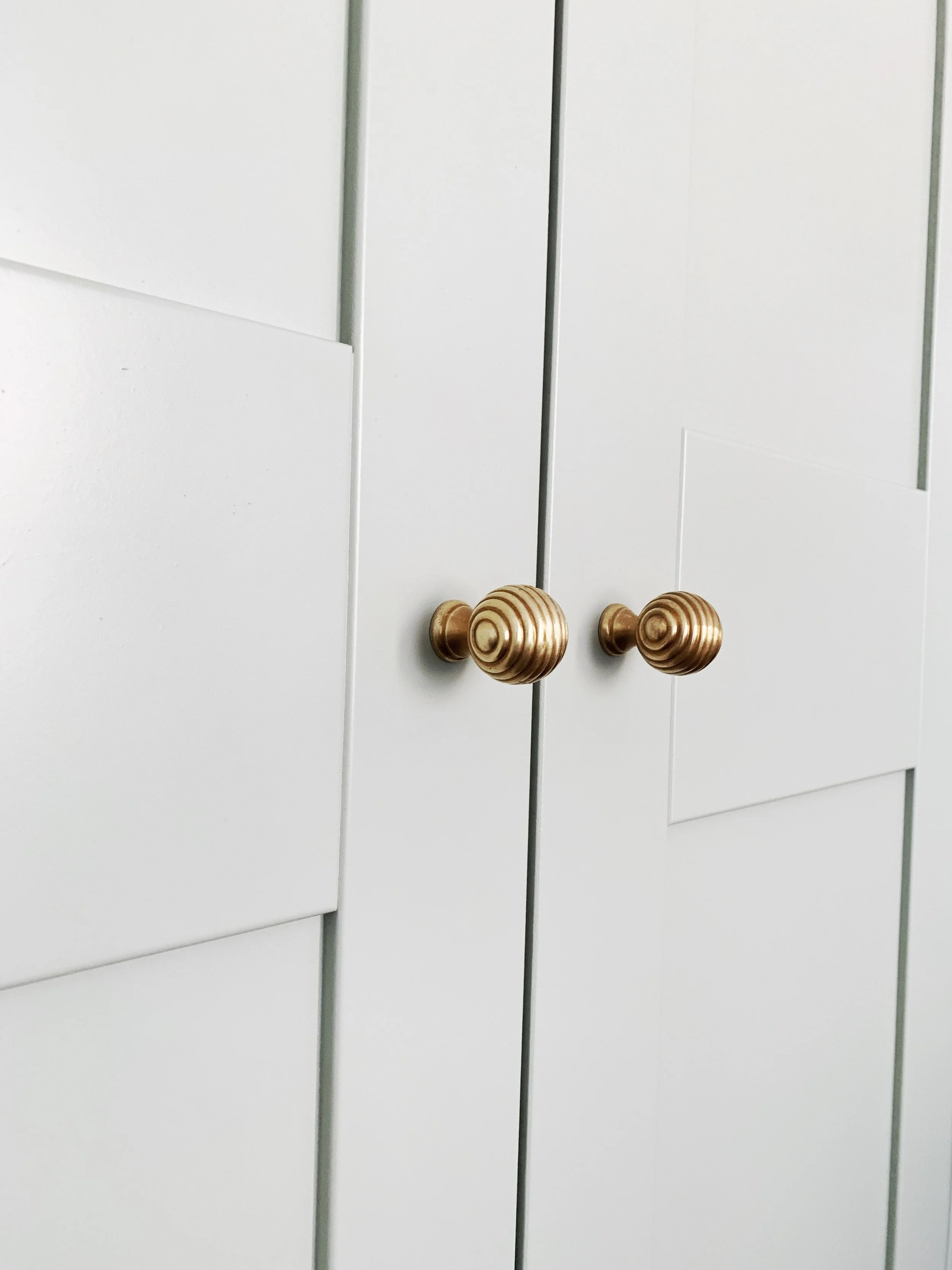 Close-up of white cabinet doors with gold, striped, spherical knobs.