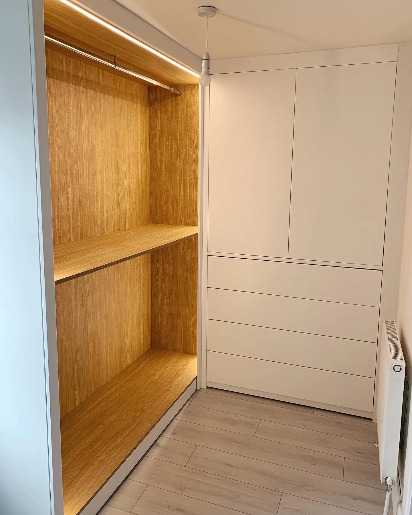 Empty built-in closet with wooden interior shelves and a white cabinet with drawers, situated against a white wall with light-colored flooring.