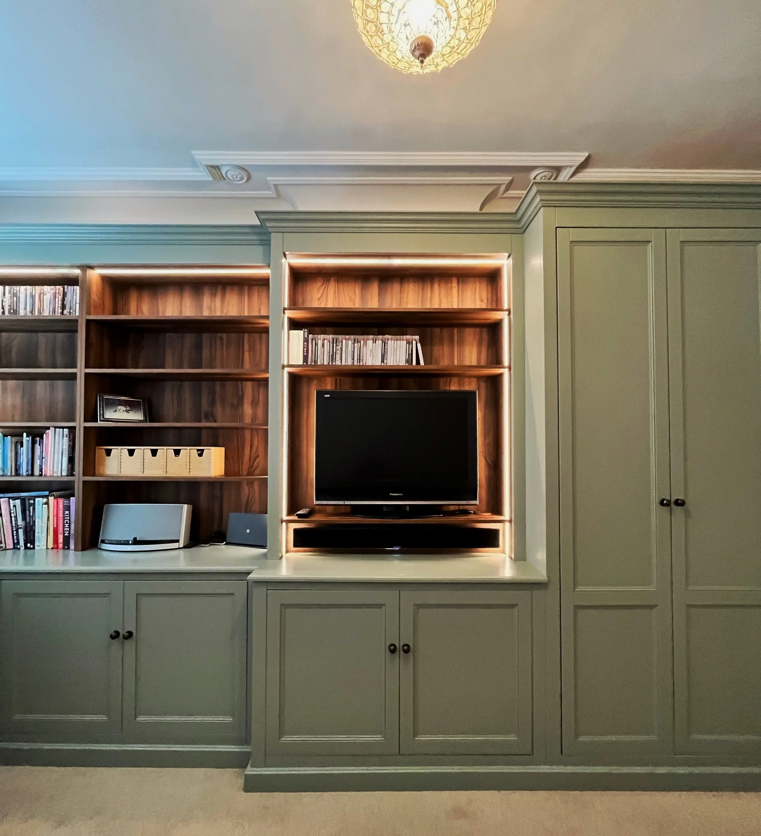 Living room with a built-in green cabinet, open wooden shelves filled with books and media, a TV, and a ceiling light fixture.