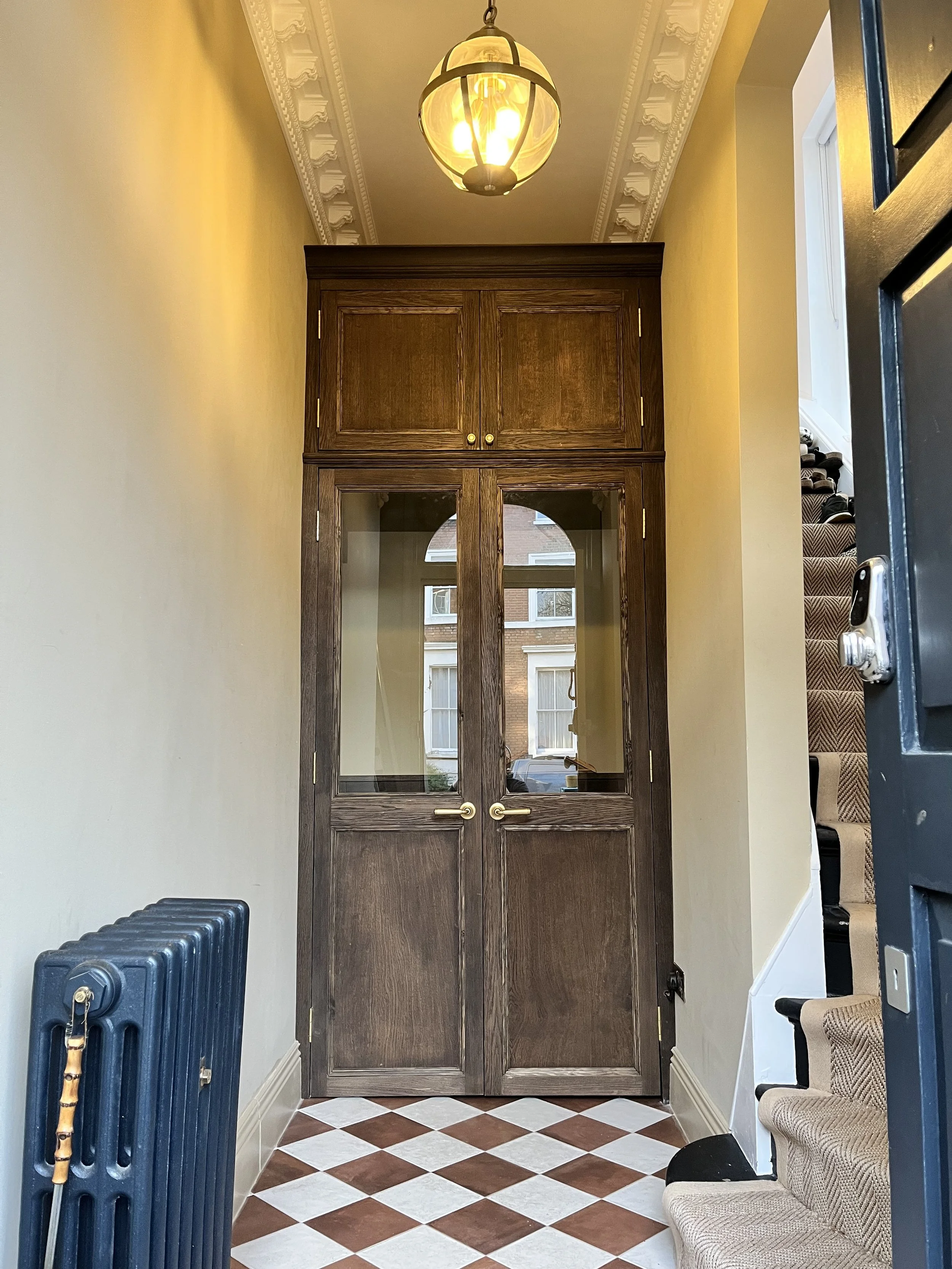View of a hallway with a wooden glass-paneled door, a staircase with carpeted steps, a black radiator, and a ceiling light fixture.