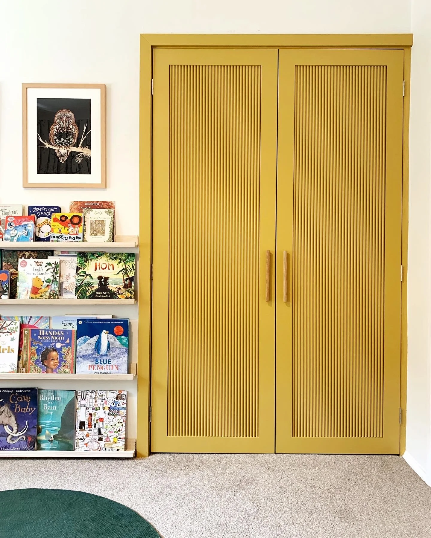 Yellow double closet doors with vertical groove design, next to a bookshelf filled with children's books, and a framed owl art above the bookshelf.