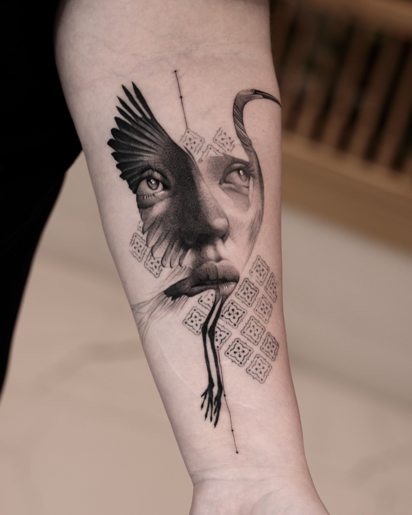 Black and grey forearm tattoo combining a crane in flight with a realistic woman’s face and geometric details.