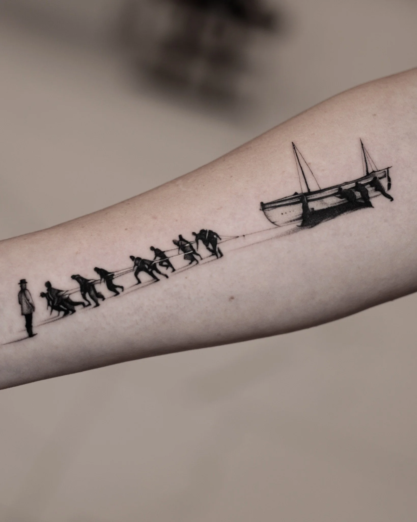Black and grey forearm tattoo of a crew hauling a boat with ropes while others push from behind.