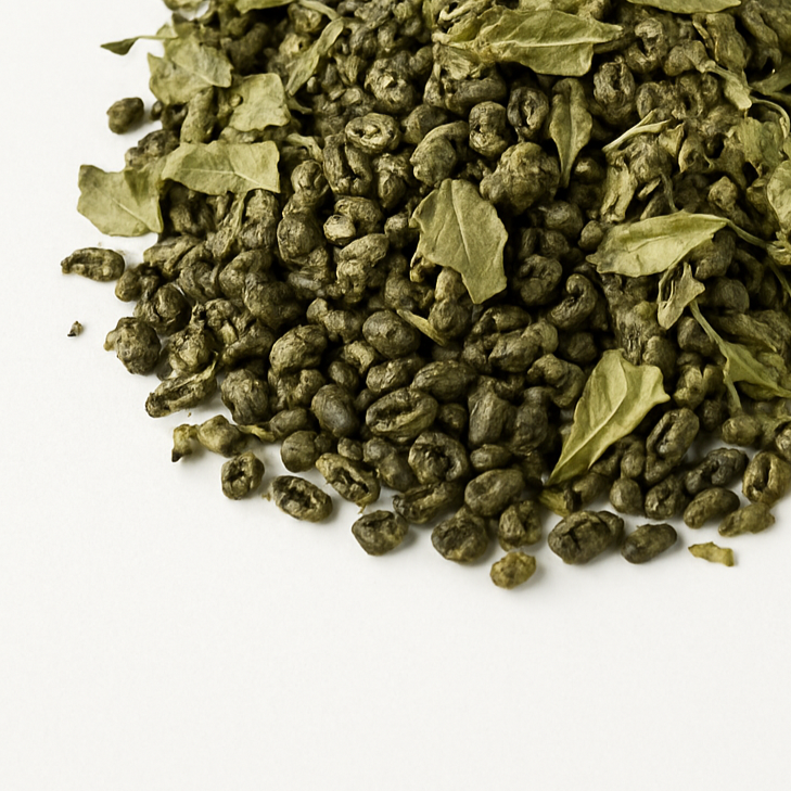 A mound of Moroccan Whiskey loose leaf tea blend on a white background featuring rolled gunpowder green tea pearls and crushed peppermint leaves — a smoky, minty handcrafted StrangeMakes herbal tea.