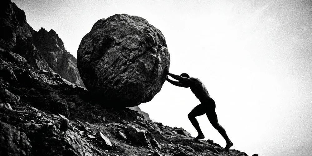 man rolling a giant boulder up a hill