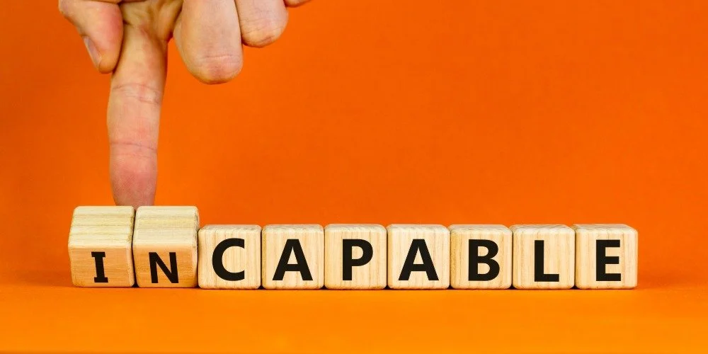 Blocks spelling out the word incapable and a hand flipping over the "in"