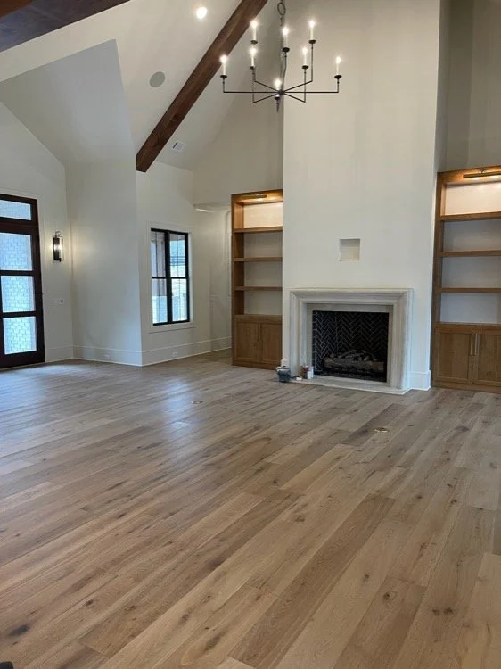 Empty living room with hardwood floors, a fireplace, built-in shelves, and a modern chandelier.