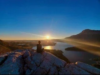 Visitor watching the sunrise from a rocky summit overlooking lakes and mountains in Glacier National Park.