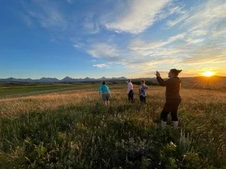 Group of visitors walking through a prairie at sunset with panoramic mountain views in Glacier National Park.