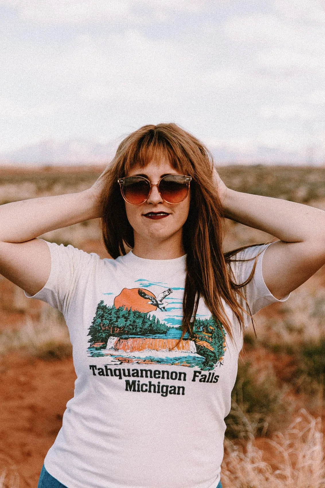 Person wearing sunglasses and a "Tahquamenon Falls Michigan" t-shirt standing outdoors.