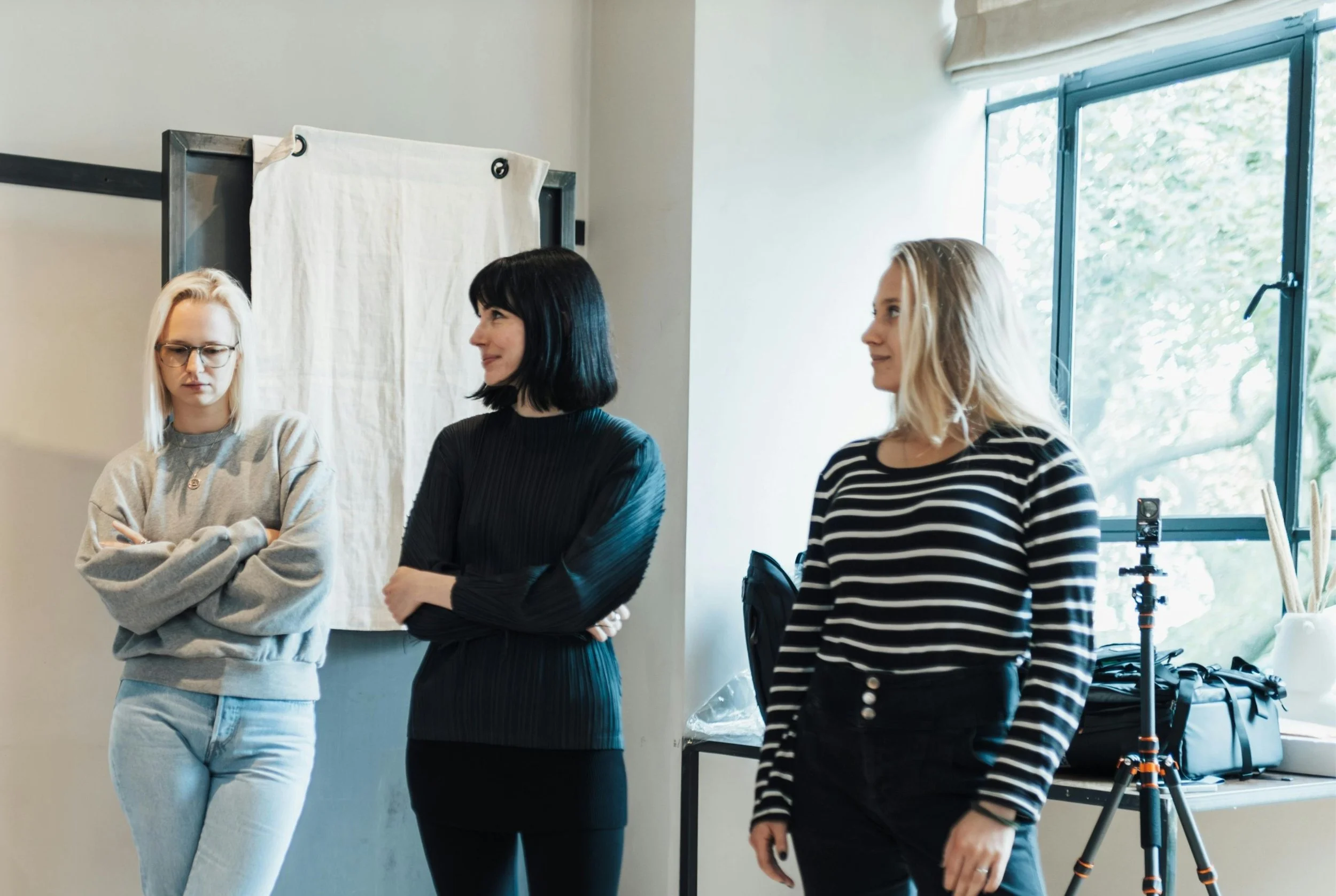 Three women are standing next to each other, each with closed body language, averted eye contact or a forced smile.