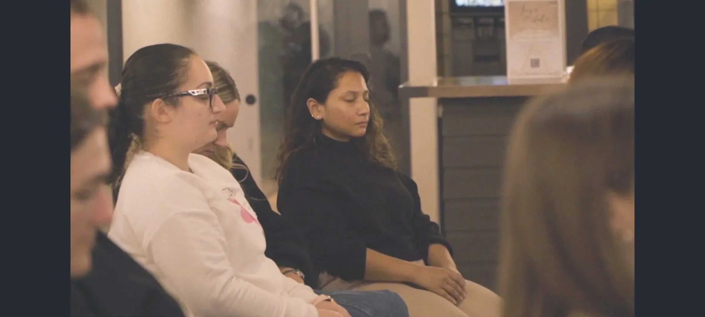Three women are seated in an audience, each has their eyes closed as they visualise an exercise the workshop leader shares with them.