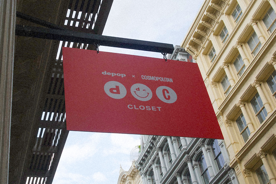 Red sign hanging on a city street, with its bright red color popping and displaying the logo and names of DEPOP and COSMOPOLITAN brands.