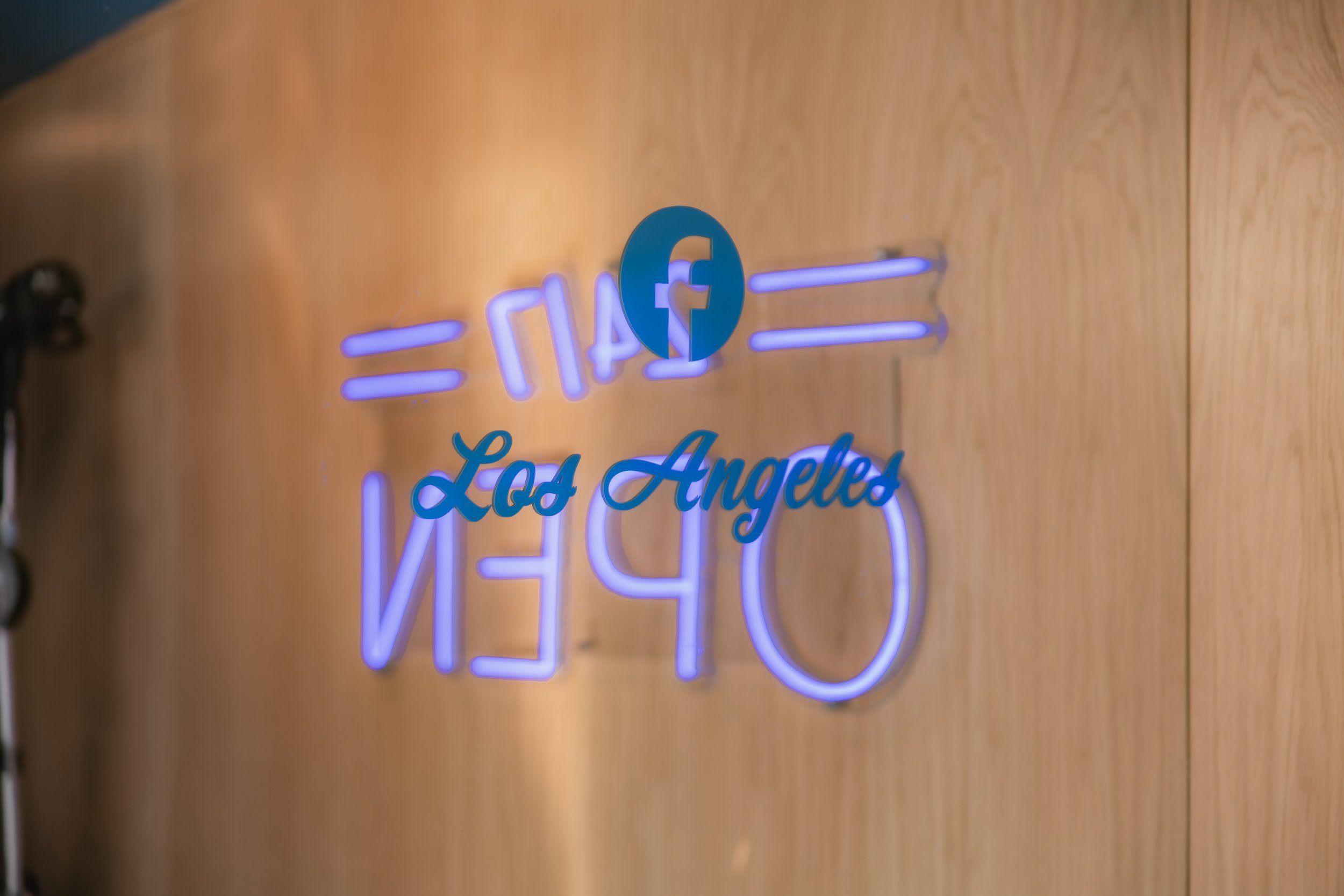 Neon sign with Facebook logo and the text 'Los Angeles' on a wooden wall.
