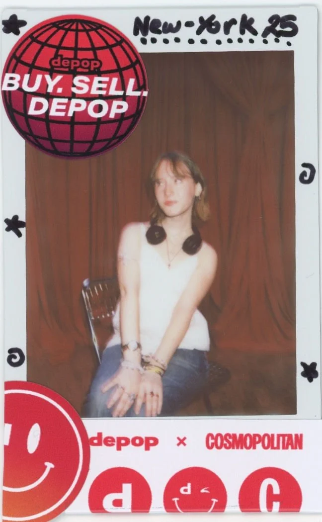 A polaroid of a young woman sitting on a chair with a wooden background. She is wearing a white sleeveless top, headphones around her neck, and multiple bracelets and rings. There are stickers on the photo with DEPOP and COSMOPOLITAN brand logos.