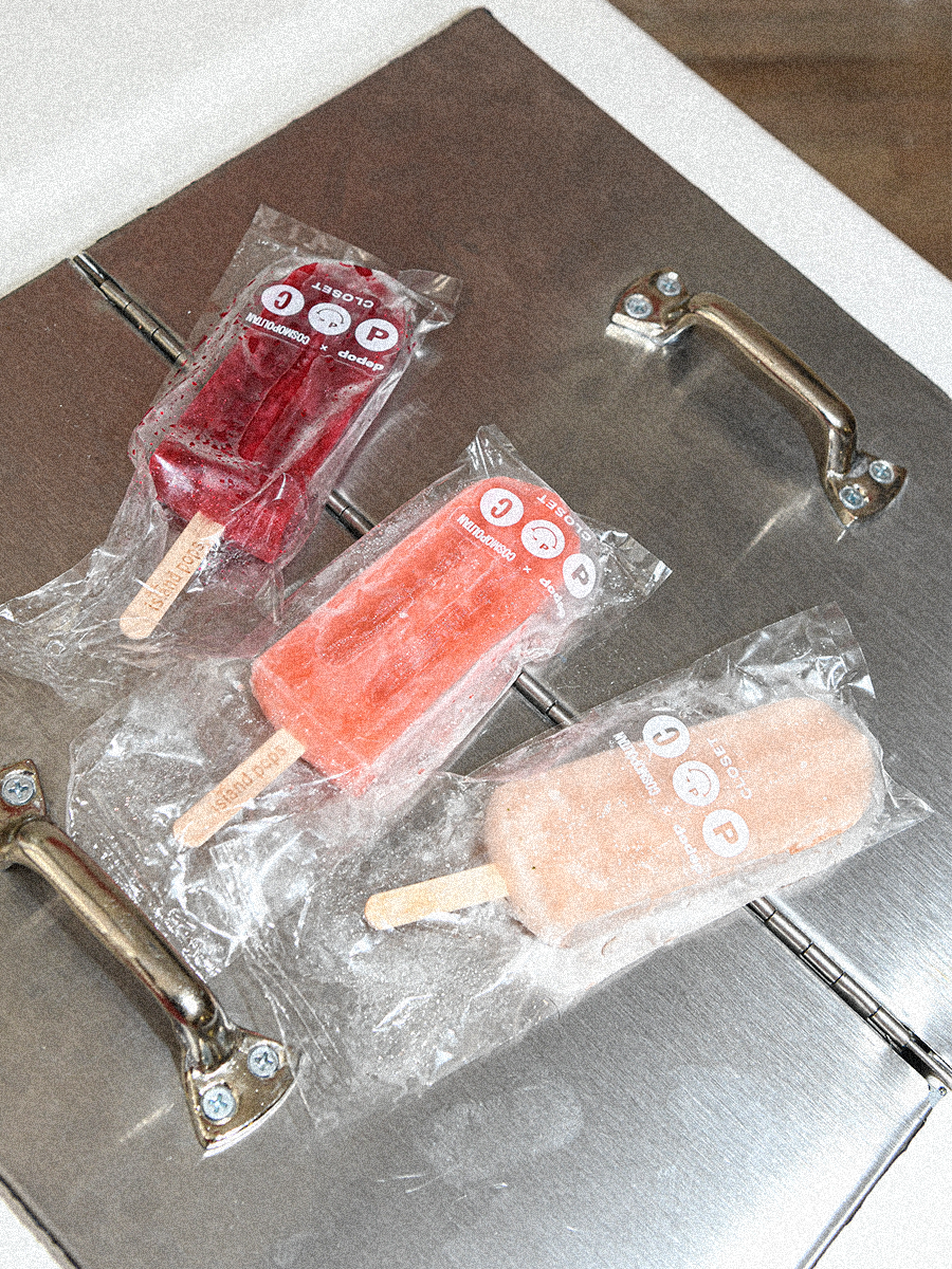 Three popsicles in plastic wrapping on a metal table with branded logos of DEPOP and COSMOPOLITAN.