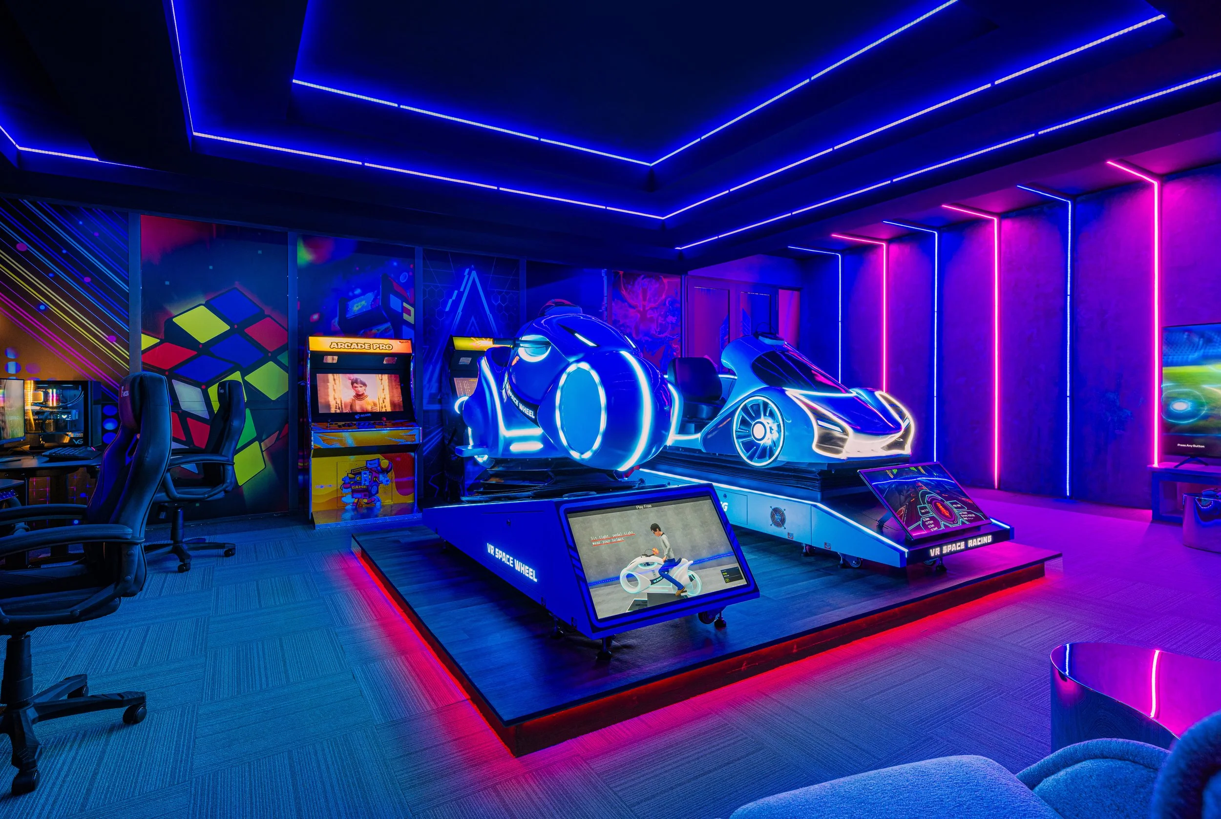 An arcade room with neon blue and pink lights, featuring a futuristic racing game with a sleek, silver racing car simulator, arcade cabinets, and gaming chairs.