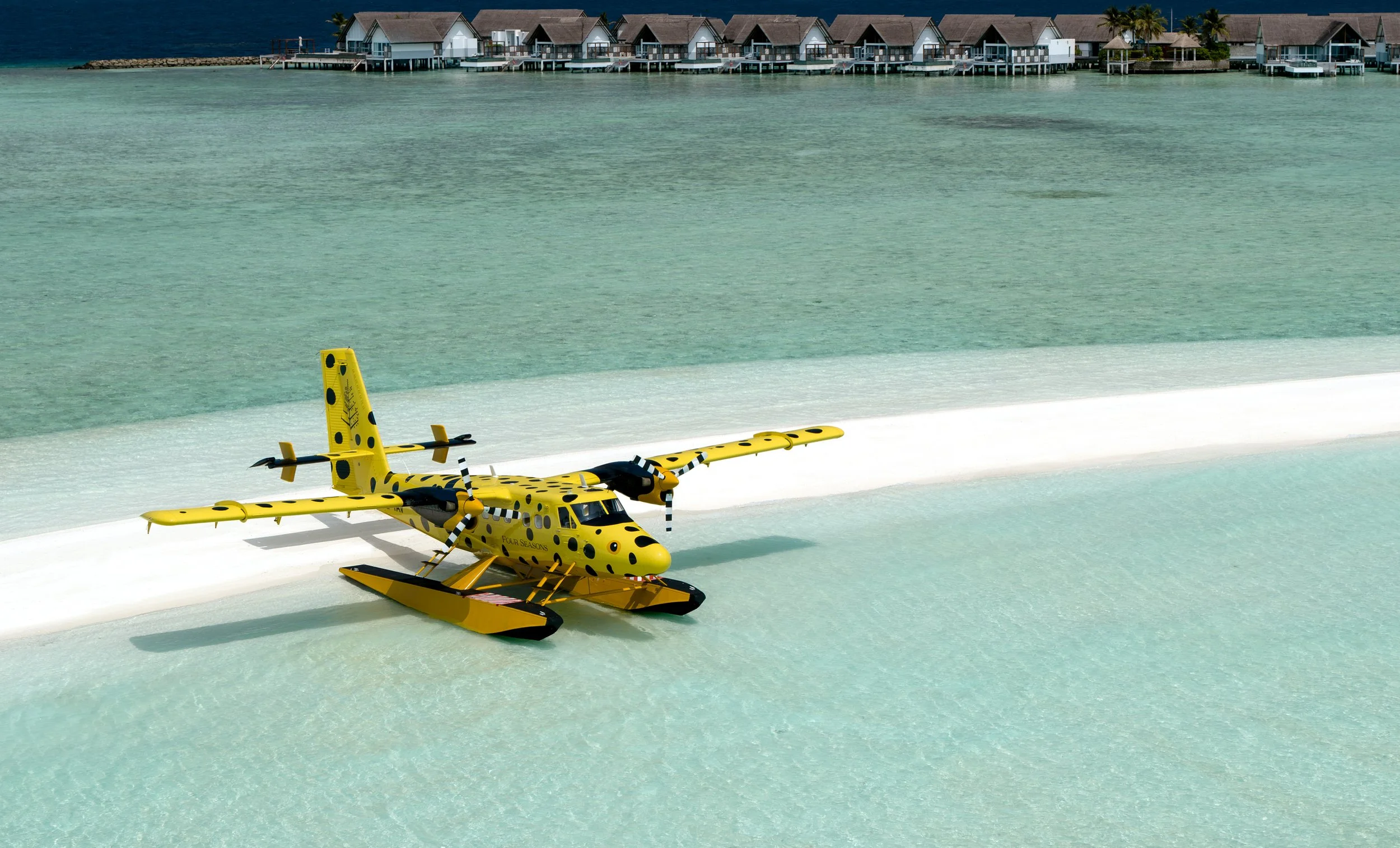 Yellow toy helicopter with black spots resembling a cheetah, placed on a white surface near the water, with overwater bungalows in the background.