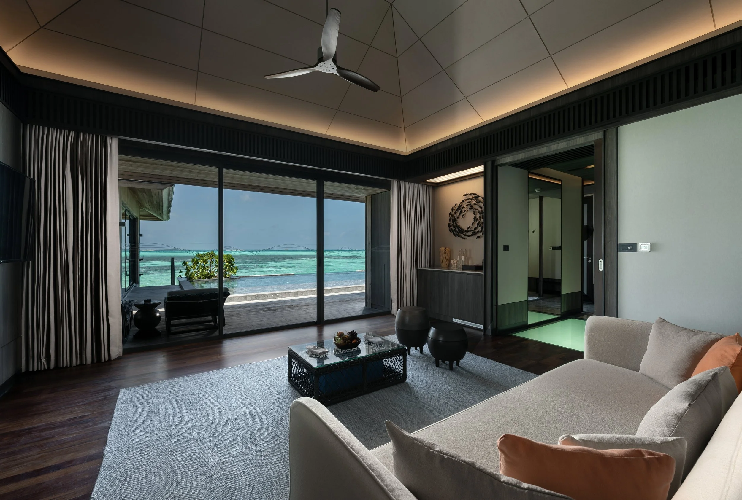 Living room with large sliding glass doors facing the ocean, modern furniture, a ceiling fan, and wooden flooring.