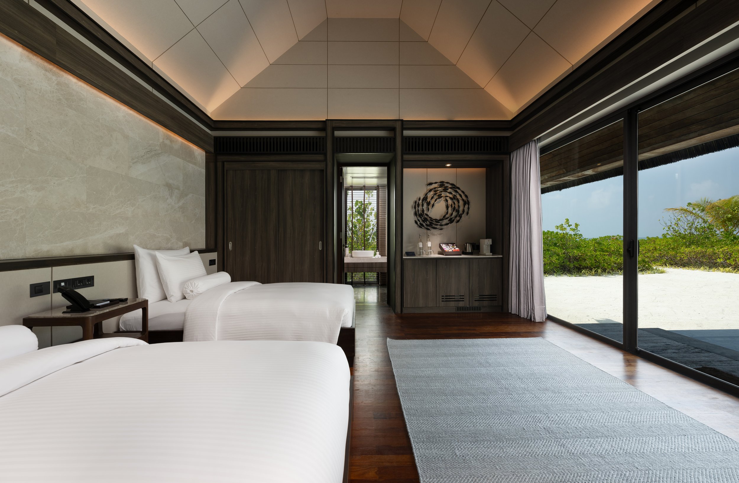 Modern bedroom with white beds and a view of greenery outside through a sliding glass door.