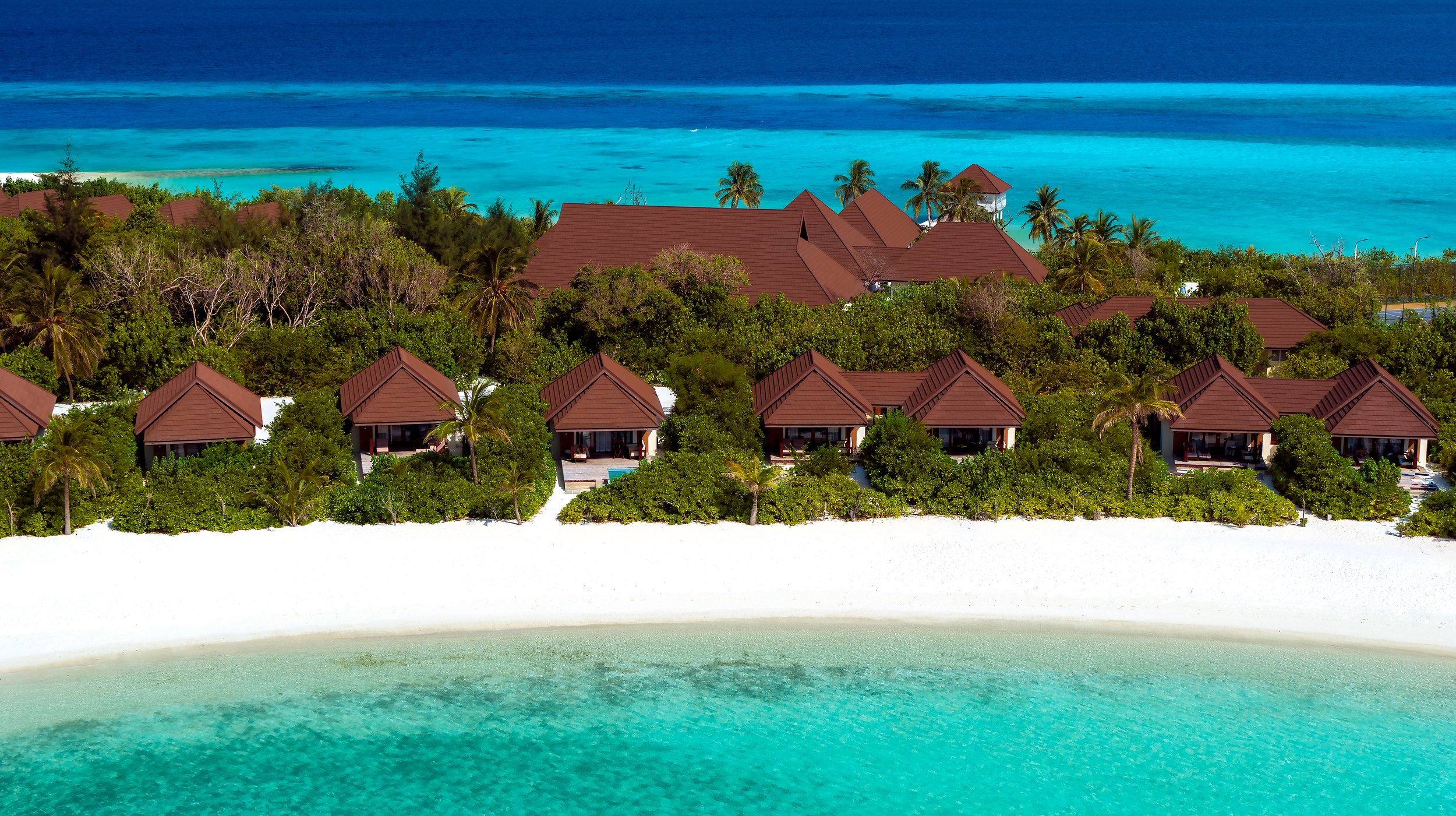 Aerial view of overwater bungalows on a tropical beach with turquoise water and lush green trees.