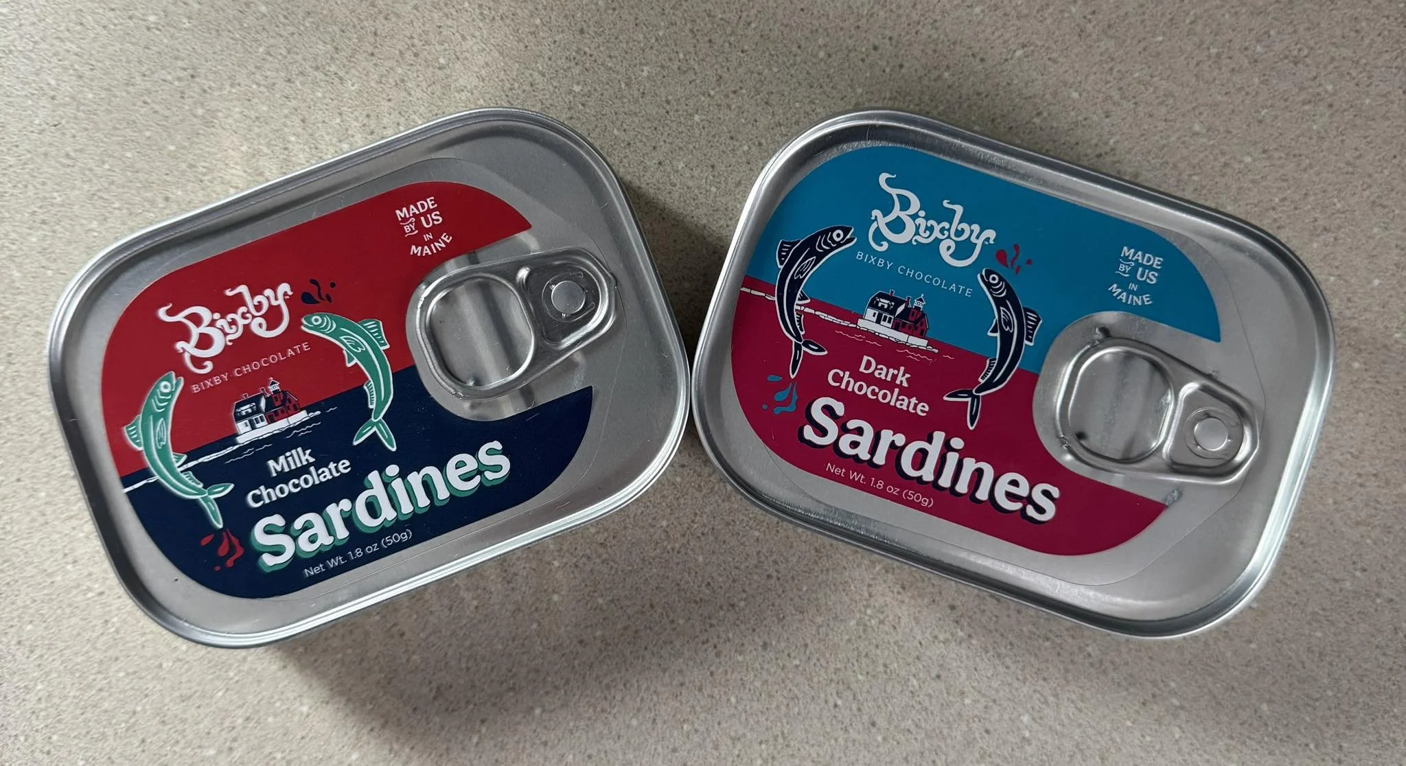 Two cans of sardines, one labeled milk chocolate and the other dark chocolate, on a kitchen countertop.