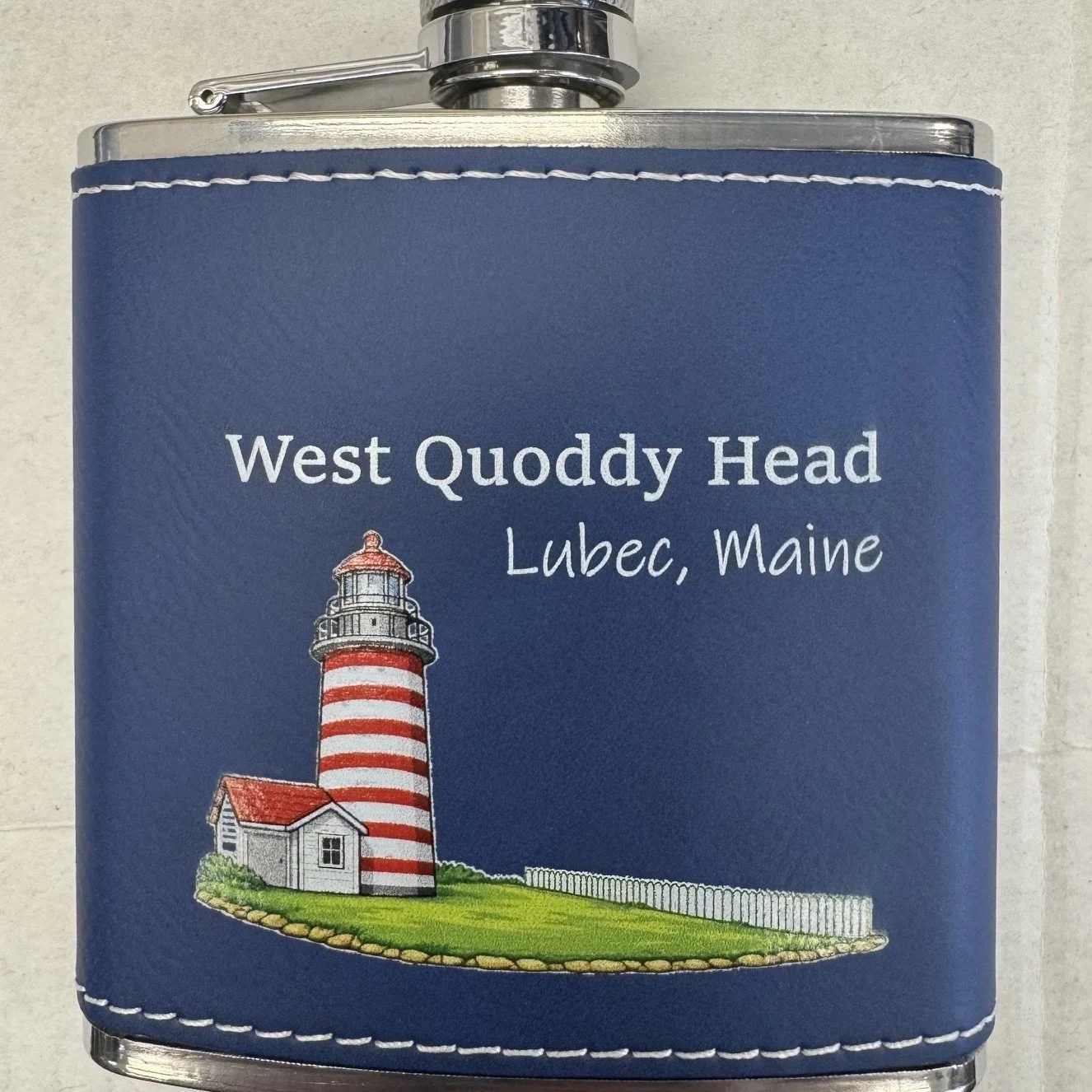 A souvenir flask with a photo of a lighthouse in Lubec, Maine, with the text 'West Quoddy Head Lubec, Maine' on a blue background.