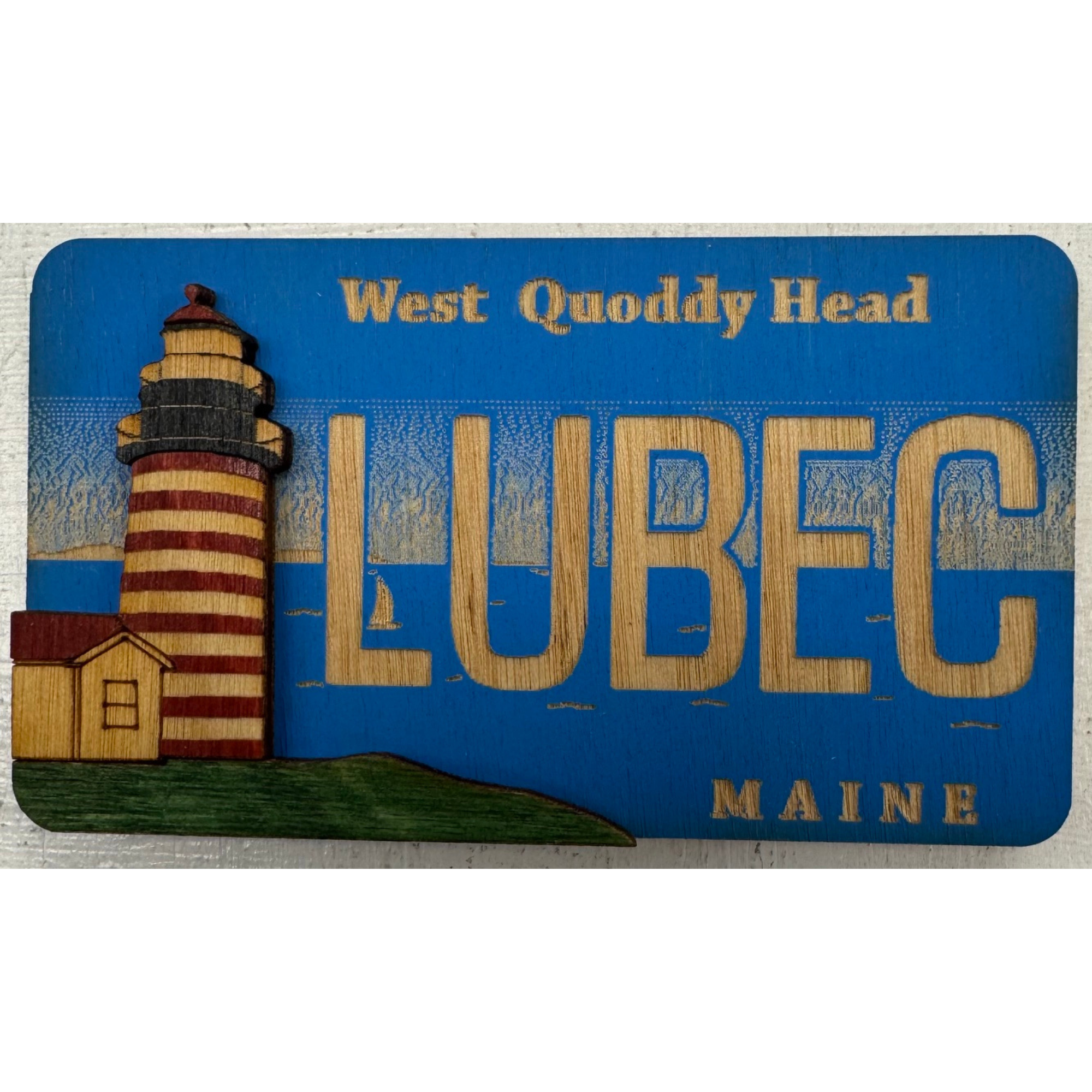 Souvenir wooden magnet with the words "West Quoddy Head" and Lubec and an illustration of a lighthouse, part of the Quoddy Head State Park in Maine.