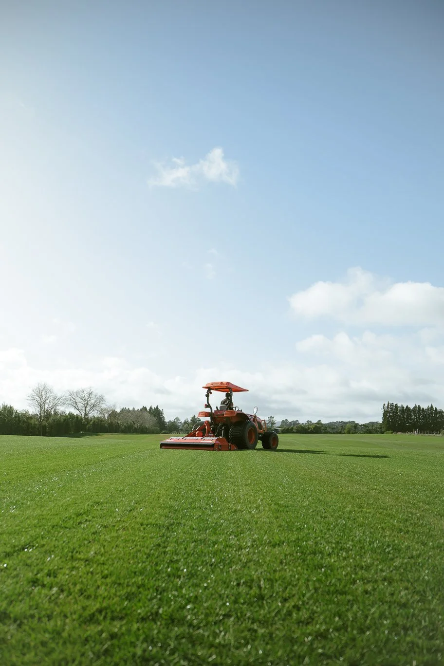 Red lawn mower cutting grass on a large, flat field with a clear blue sky and a few clouds.