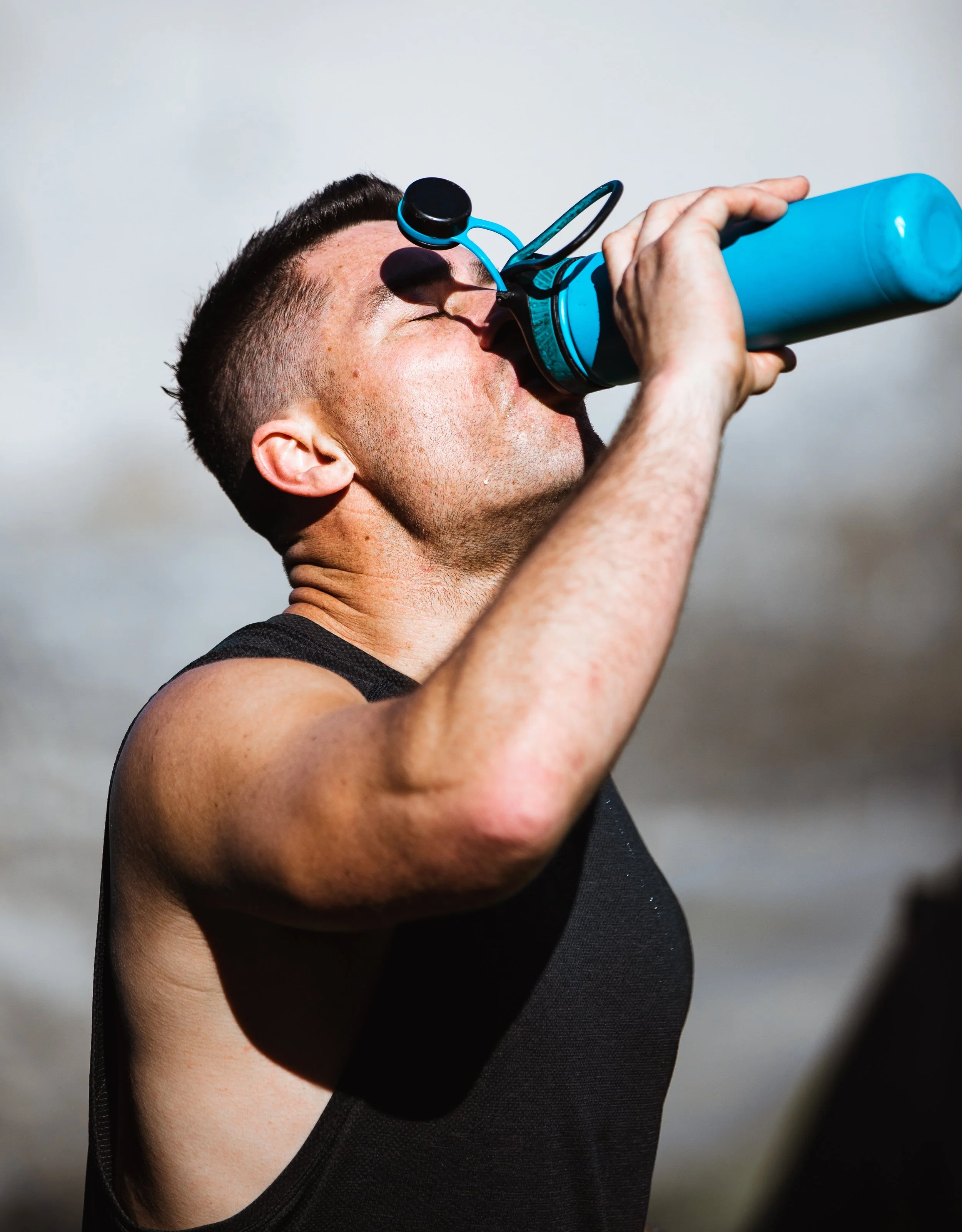 Man in black tank top drinking water from blue water bottle