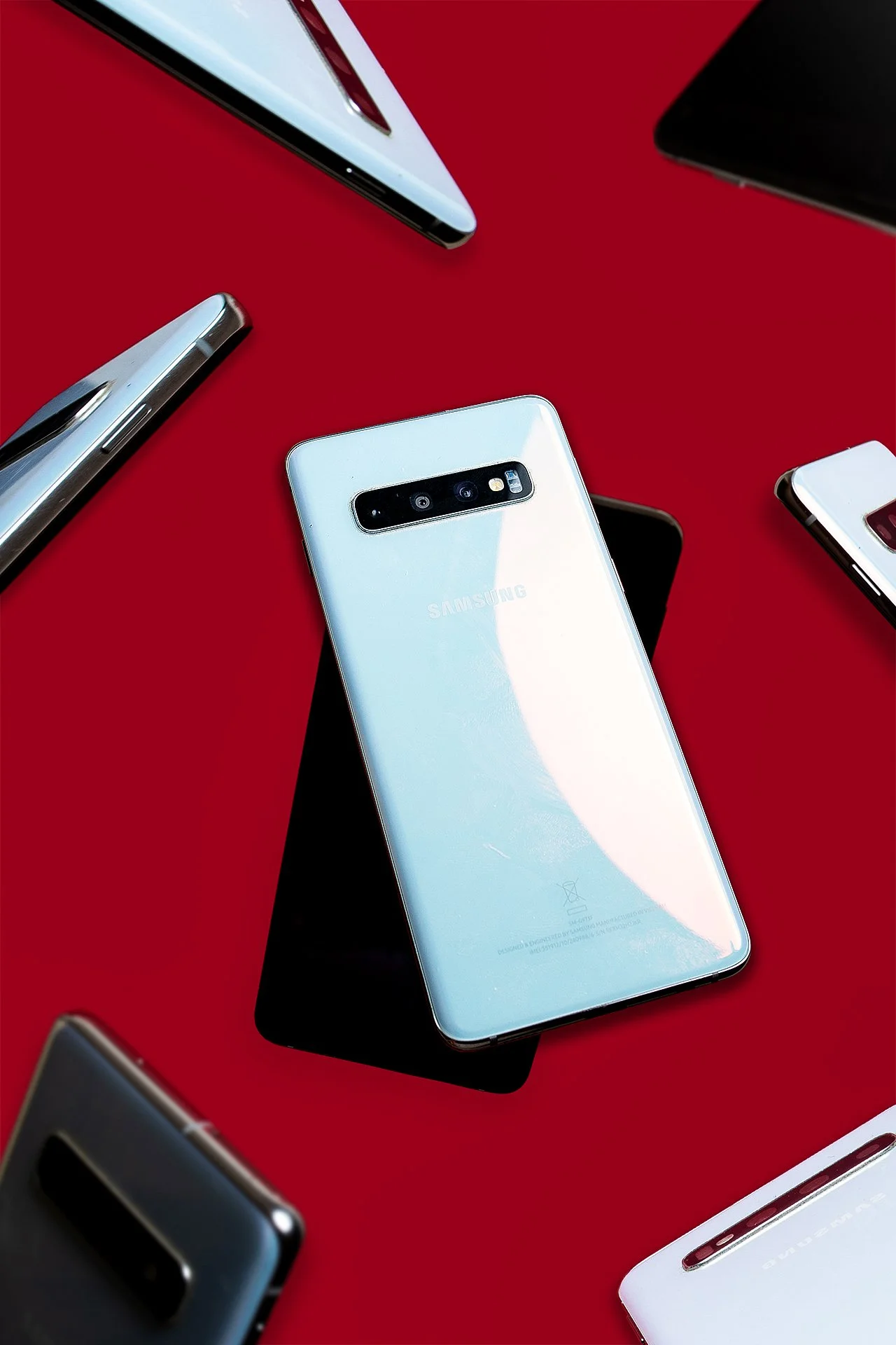 Multiple smartphones, including a Samsung phone, placed on a red surface.