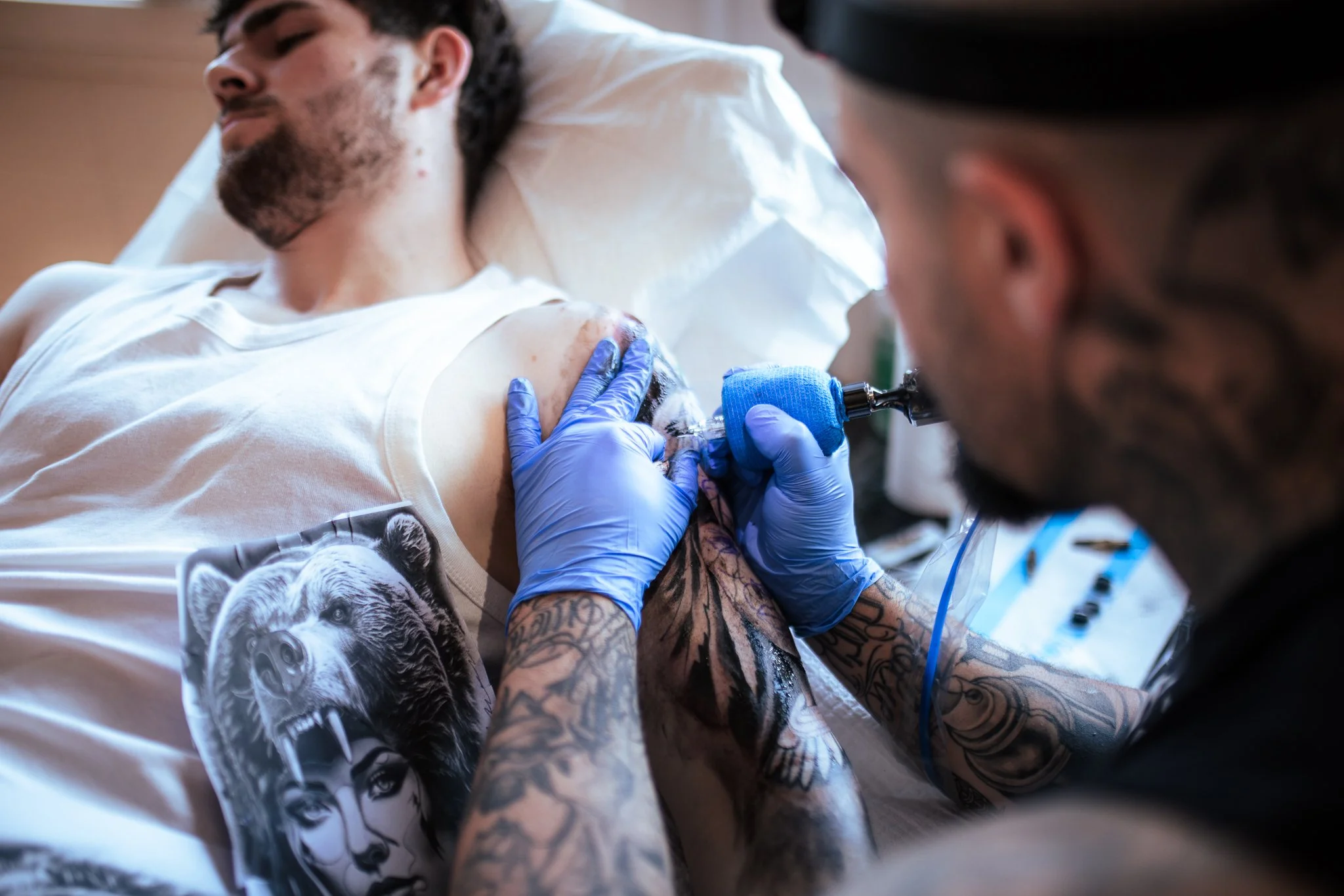 A tattoo artist in gloves is tattooing a man's arm in a tattoo parlor.