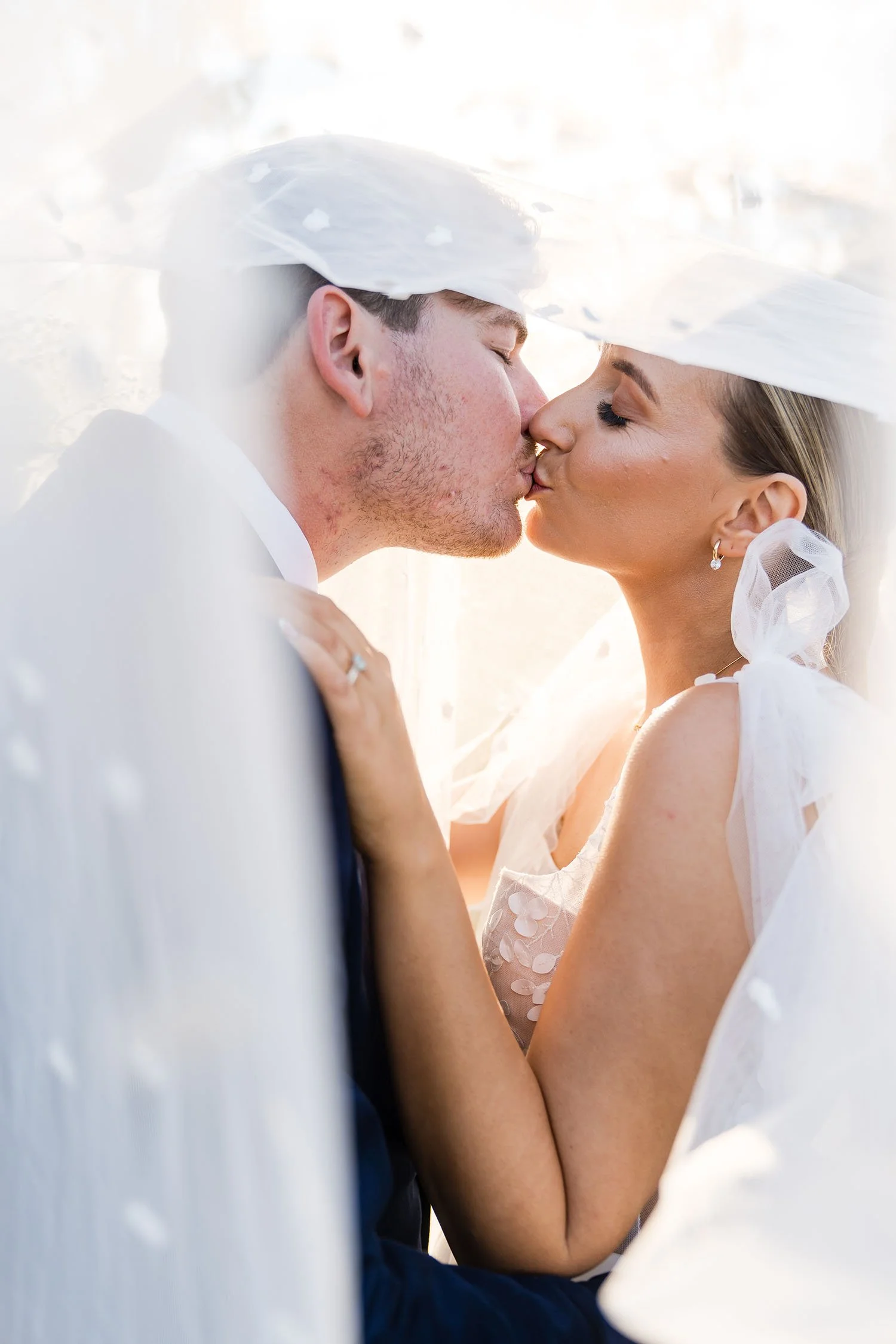 bride and groom kiss at golden hour under a veil