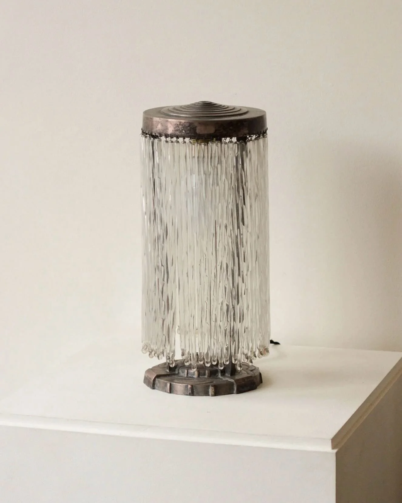 A table lamp in silvered bronze and baguette glass fringed pendants, with geometric decoration to the base and top.

France, C1925.