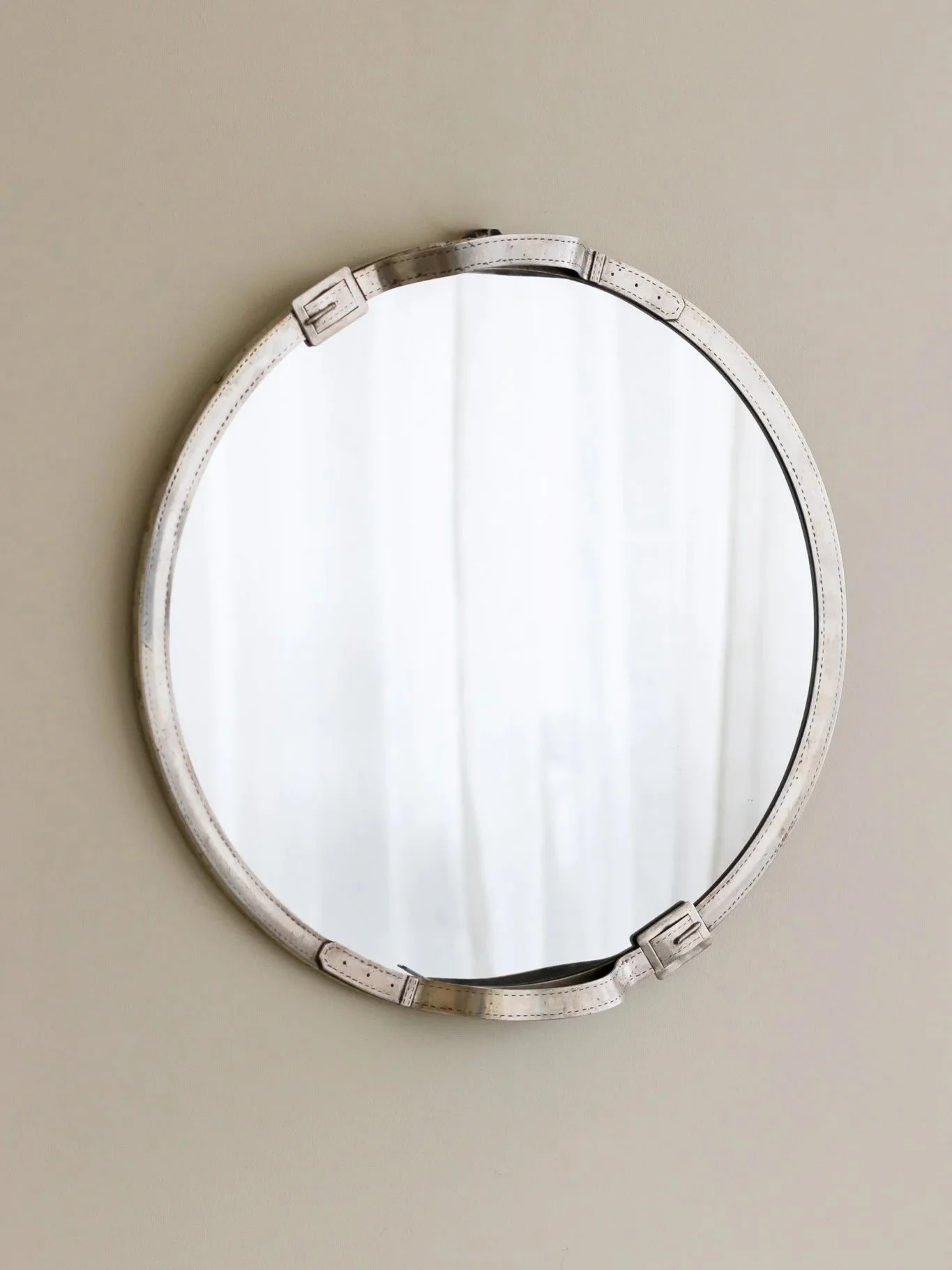 Now available; a silver plated brass round wall mirror with trompe l&rsquo;oeil relief buckle decoration at the top and bottom, in the manner of Maria Pergay.

France, C1950.

Diameter: 55cm