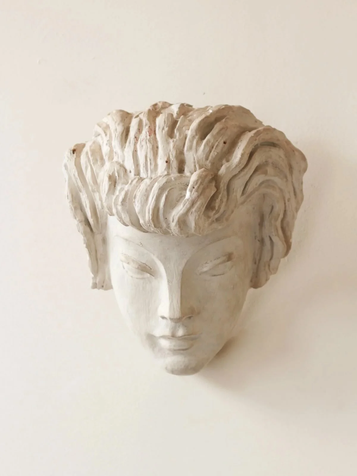 A wall mounted sculptural mask depicting the head of a classical female face with stylised hair.

French, C1940.

Height: 25cm
Width: 20cm
Depth: 12cm