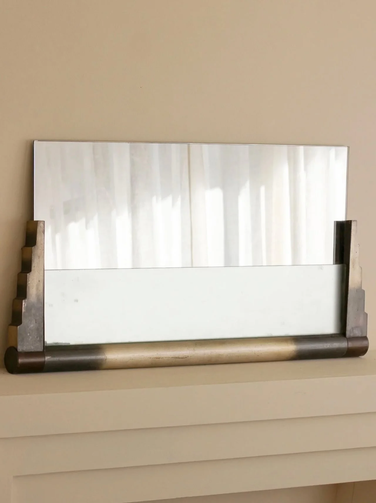 An Art Deco horizontal wall or mantel mirror featuring stepped, geometric side supports and a contrasting metallic tubular base.

With a panel of frosted glass to diffuse light at the front, as the mirror originally was designed to be wired to light 