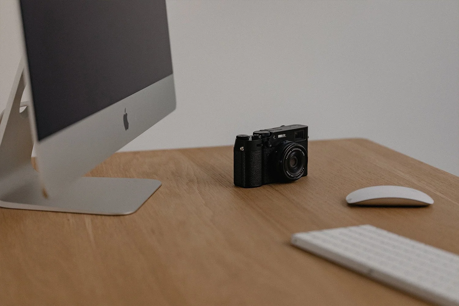 Kauniin työpöydän päällä on Applen iMac tietokone, näppäimistö, hiiri sekä musta digikamera.