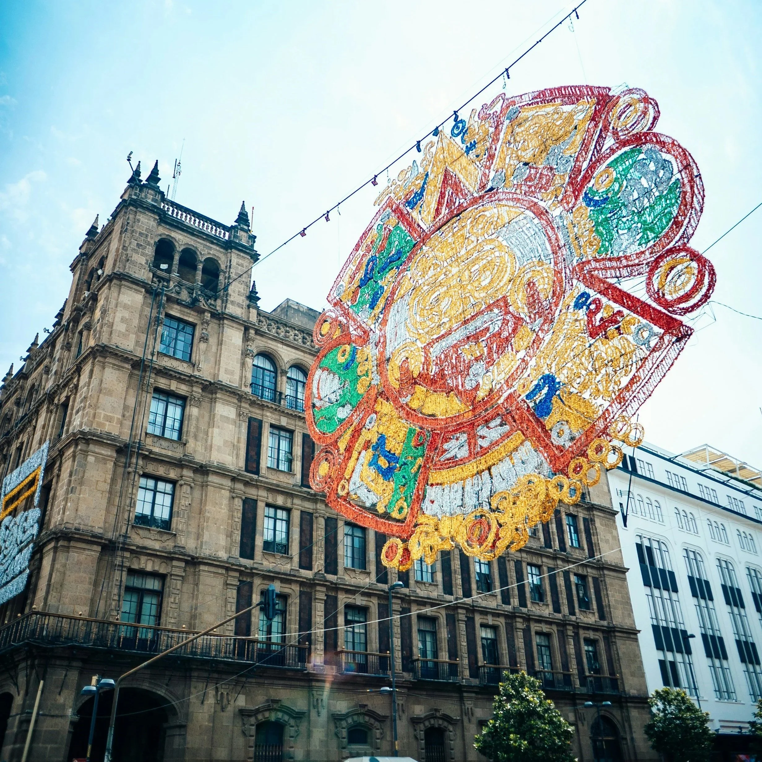 Colorful decorative street installation hanging above a historic street in Mexico City.