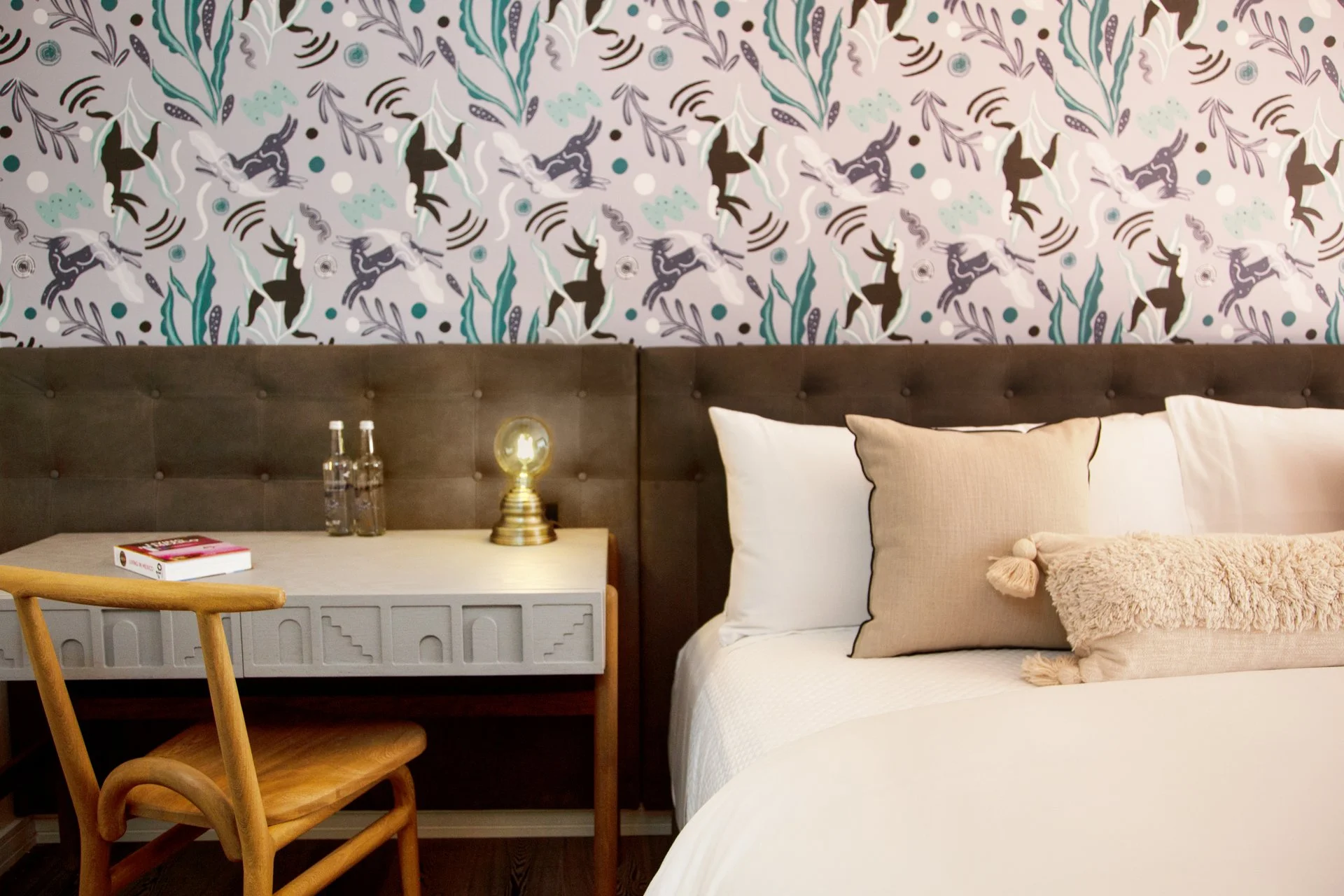 Modern hotel room with white bedding, floral accent wall, and wooden desk