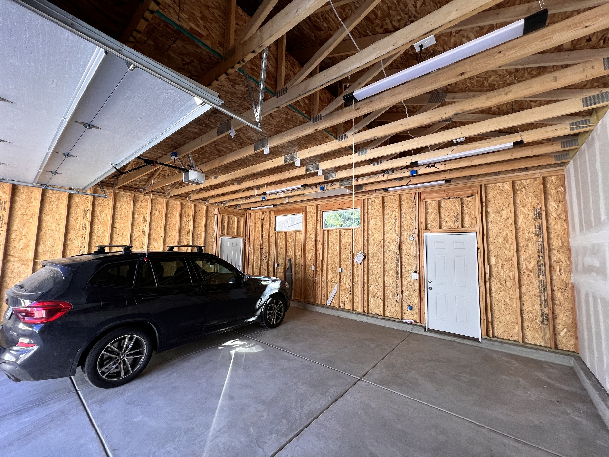 Interior of a newly built custom garage in Denver, Colorado, featuring open roof trusses designed for attic storage, finished concrete slab flooring, and integrated lighting by Prenvalley Builders.