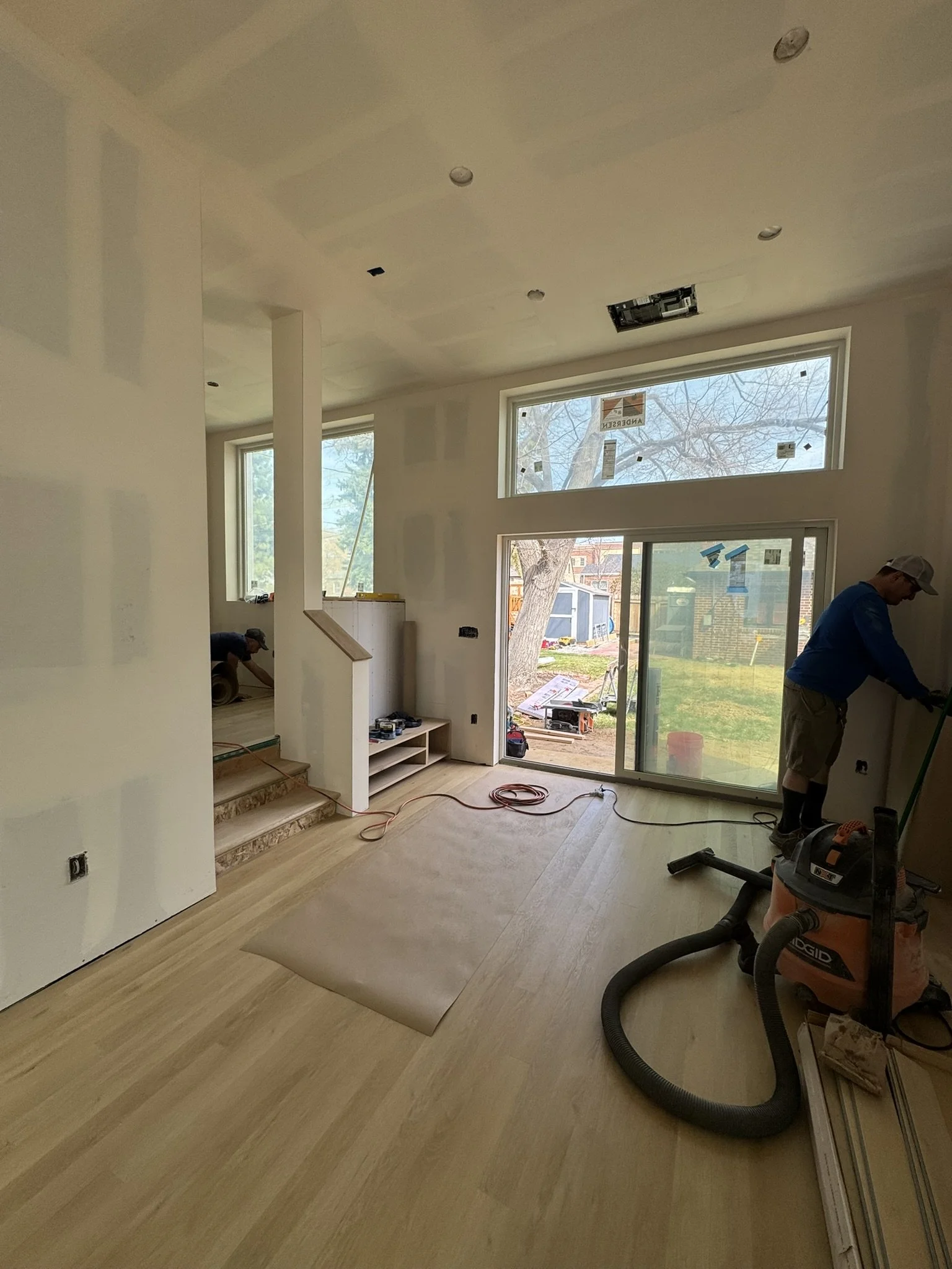 Interior view of a Denver home addition during finishing phase, featuring new hardwood flooring, high ceilings, large windows, and sliding glass doors installed by Prenvalley Builders.
