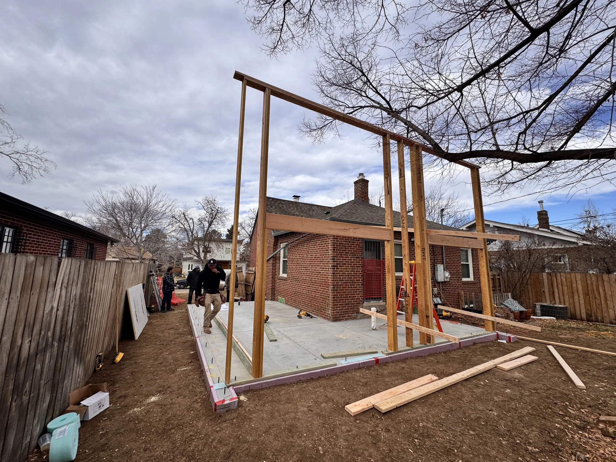Structural framing underway for a Denver home addition, with new wall framing rising from a concrete slab alongside an existing historic brick home by Prenvalley Builders.