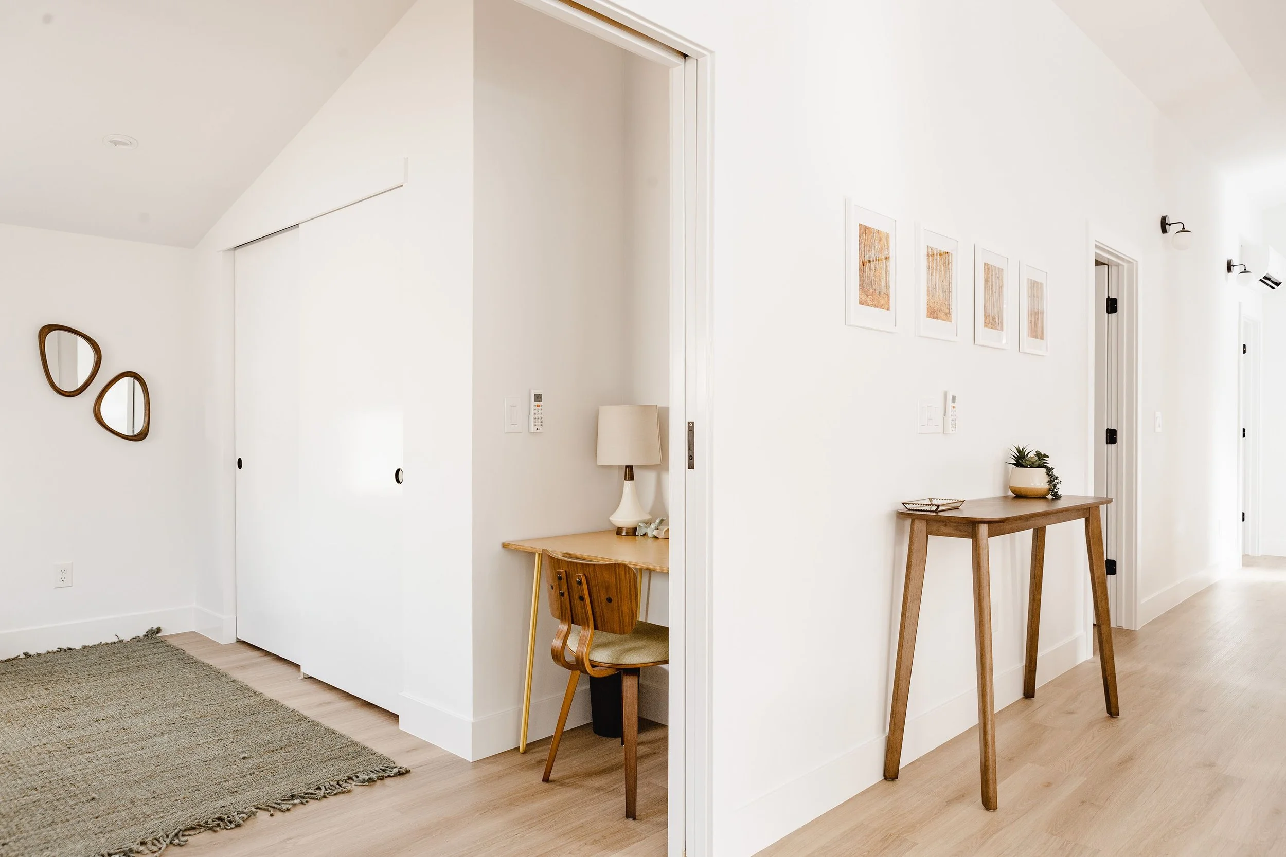 Modern Denver ADU hallway featuring a built-in desk nook, sliding closet doors, light wood flooring, and minimalist storage by Prenvalley Builders.