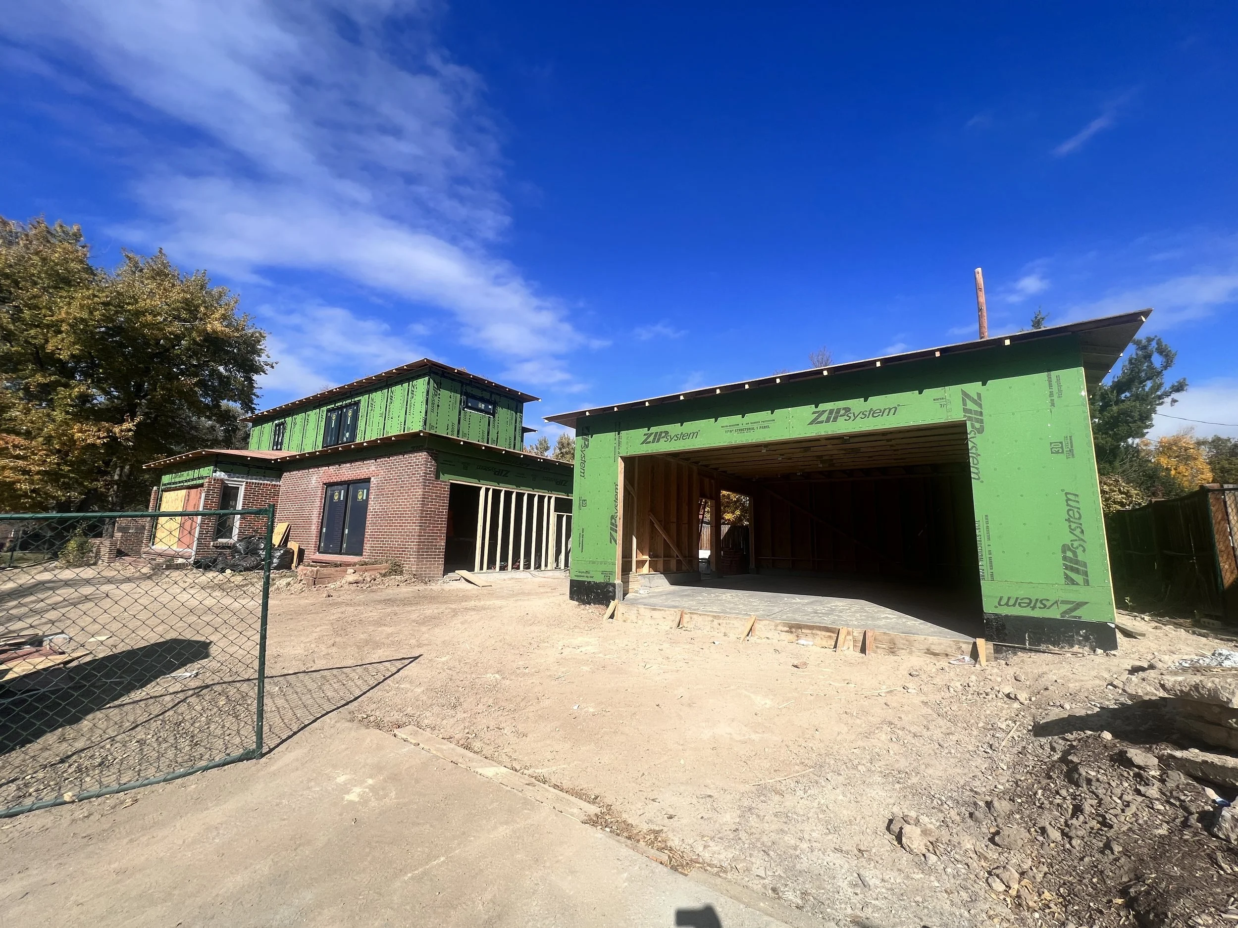 Construction phase of a Denver pop-top renovation showing second-story framing and detached garage structure in progress