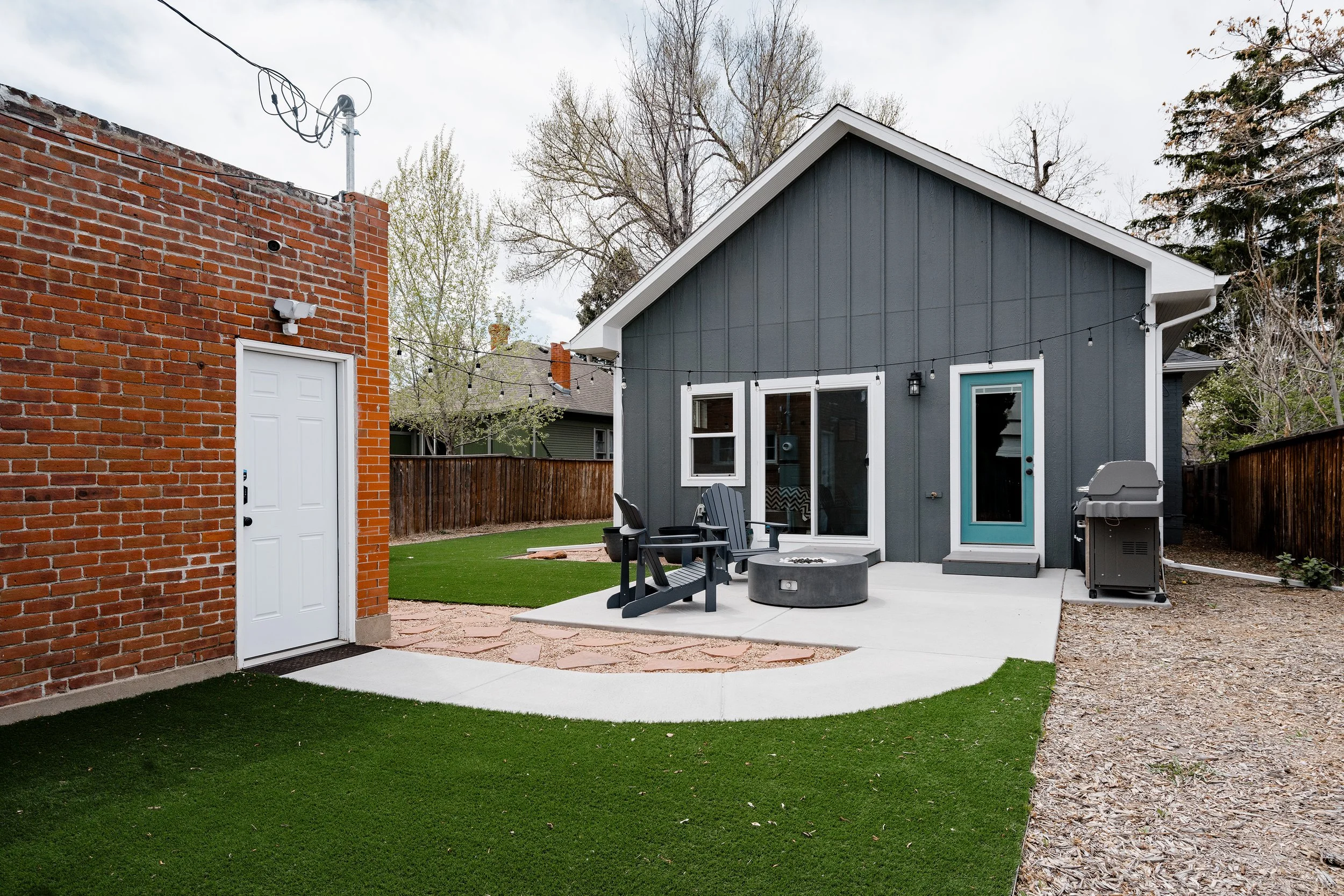 Full backyard view of a Denver home addition showing a new primary-suite structure with board-and-batten siding, concrete patio, and integrated outdoor living area.