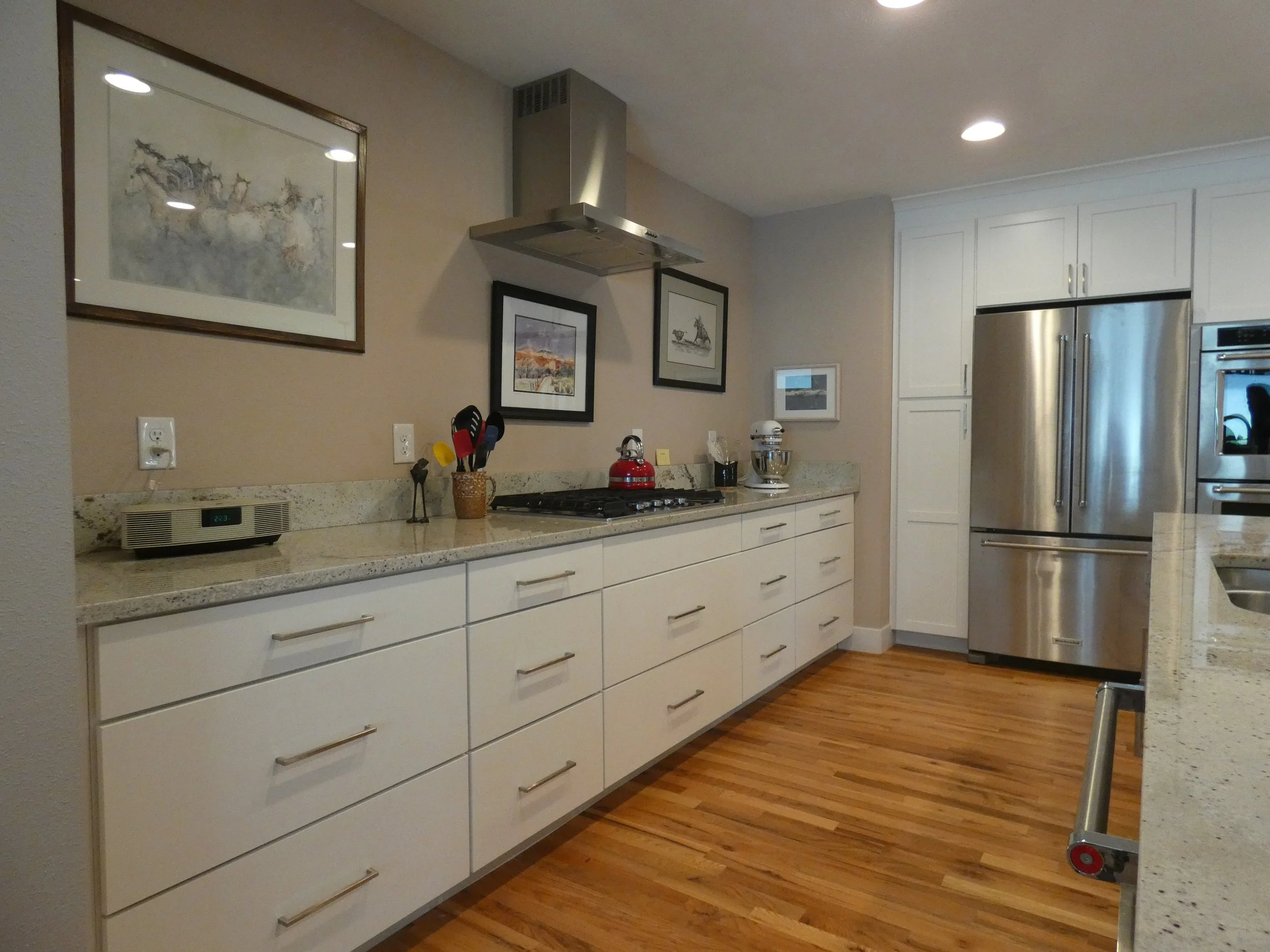 Completed kitchen after renovation in a Denver home, featuring white cabinetry, stone countertops, stainless steel appliances, and hardwood floors built by Prenvalley Builders.